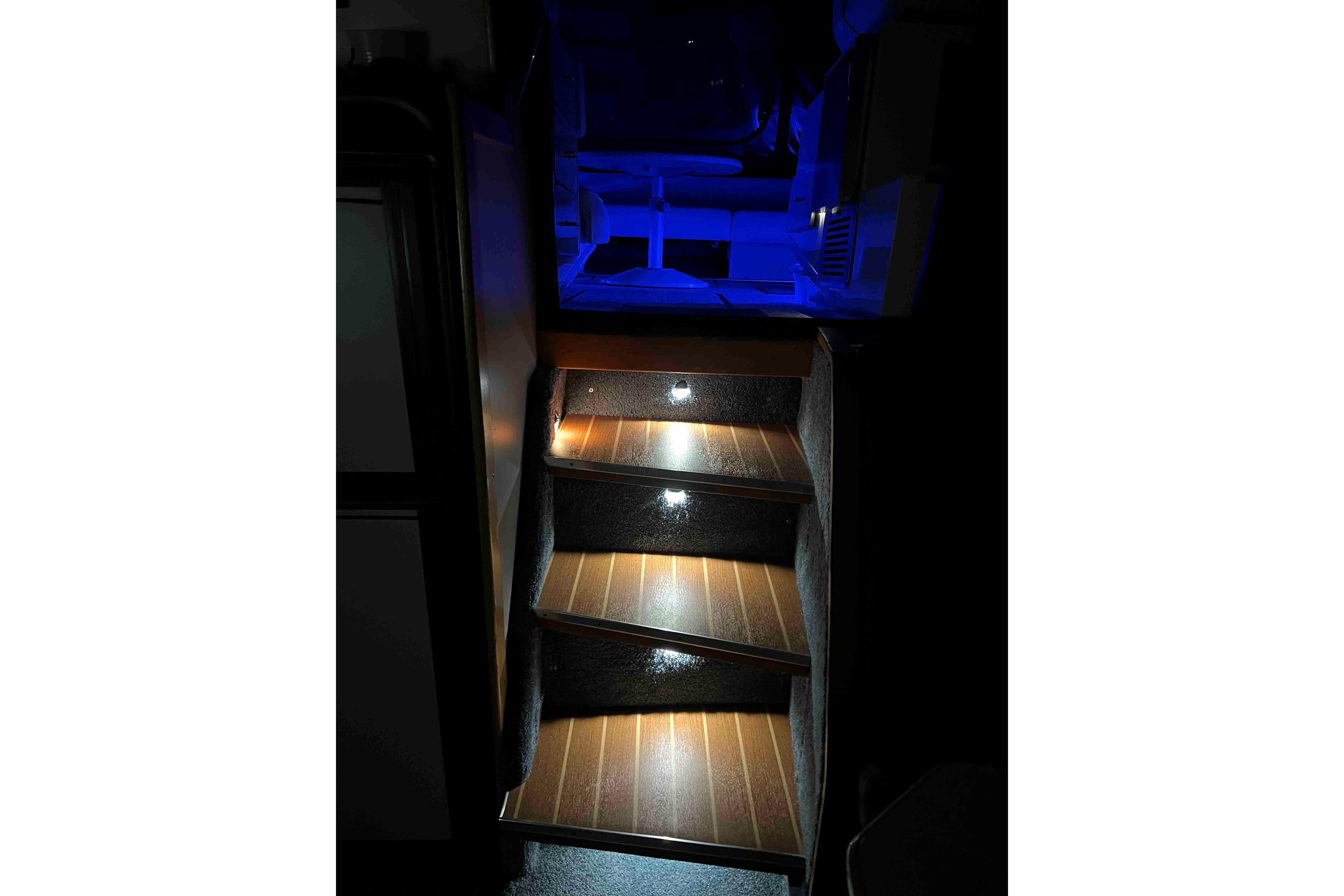 Illuminated wooden steps inside a 1991 Sea Ray 390 Express Cruiser, featuring blue ambient lighting.