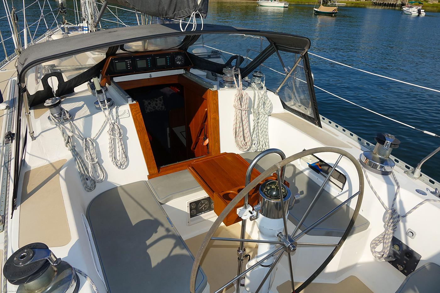 Cockpit of 1989 Nordic 40 sailboat with steering wheel and ropes, docked on calm water.