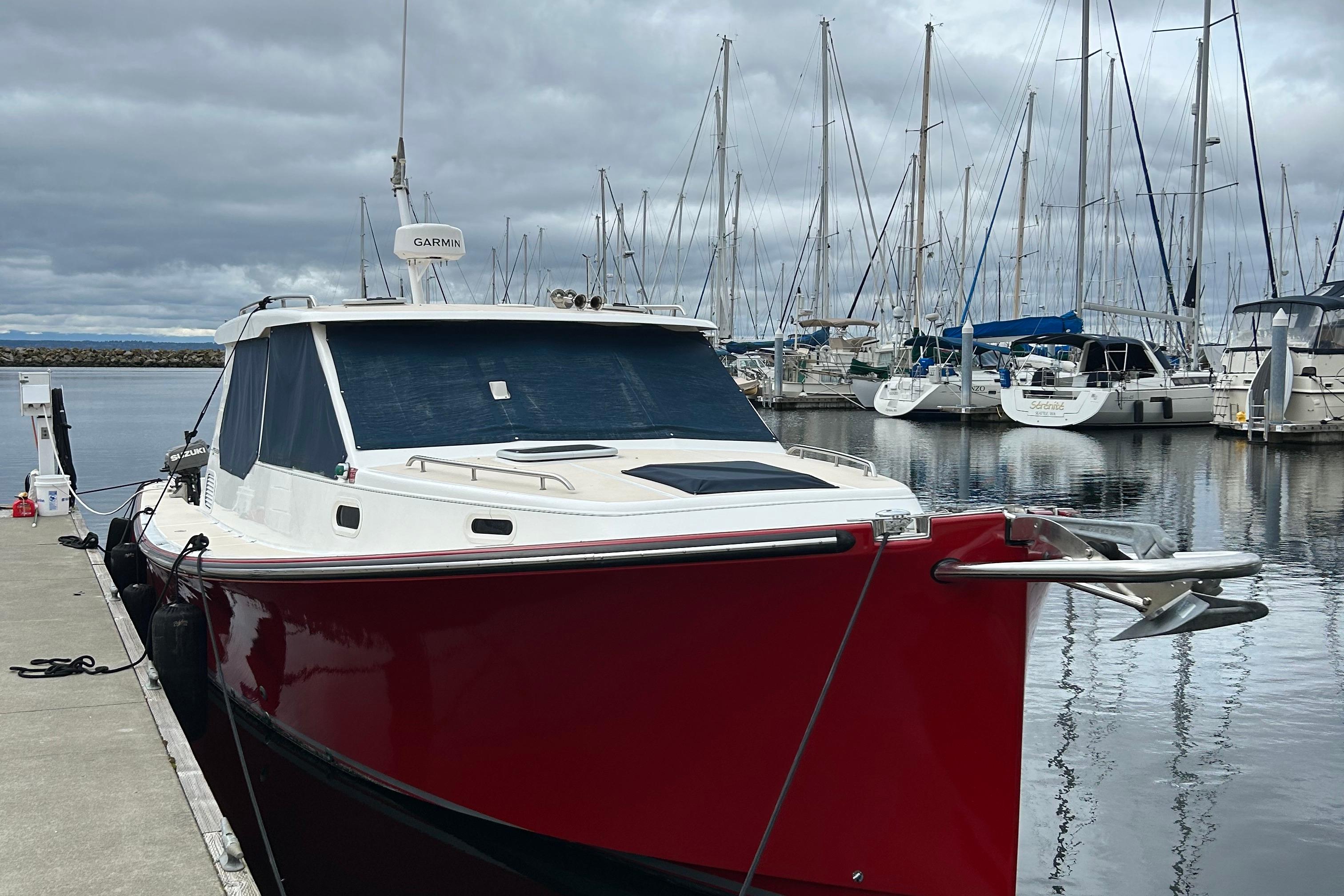 Red 2002 True North 38 boat docked at marina with sailboats in background.