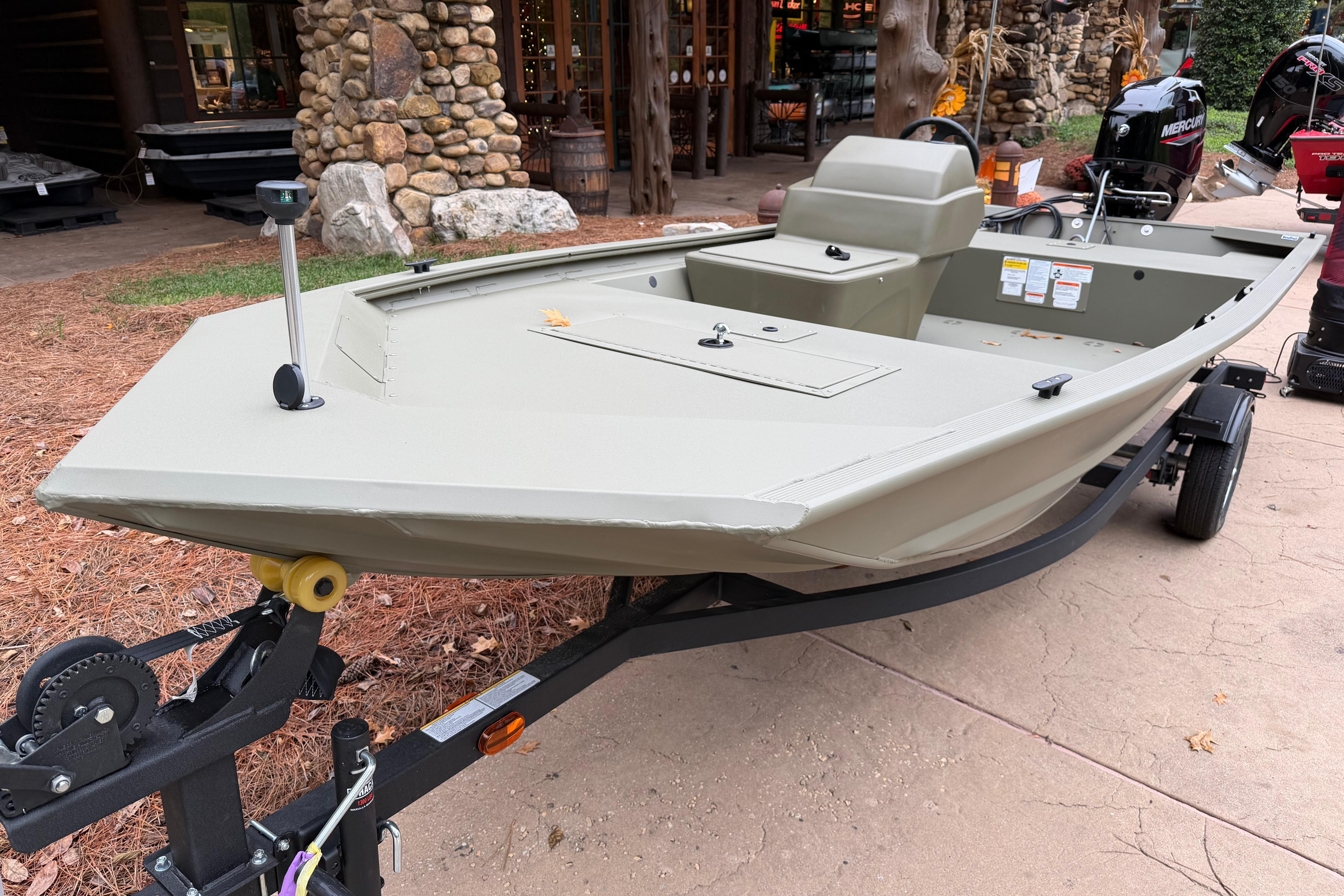 2026 Tracker Grizzly 1648 SC boat on trailer, parked outdoors near rustic building.