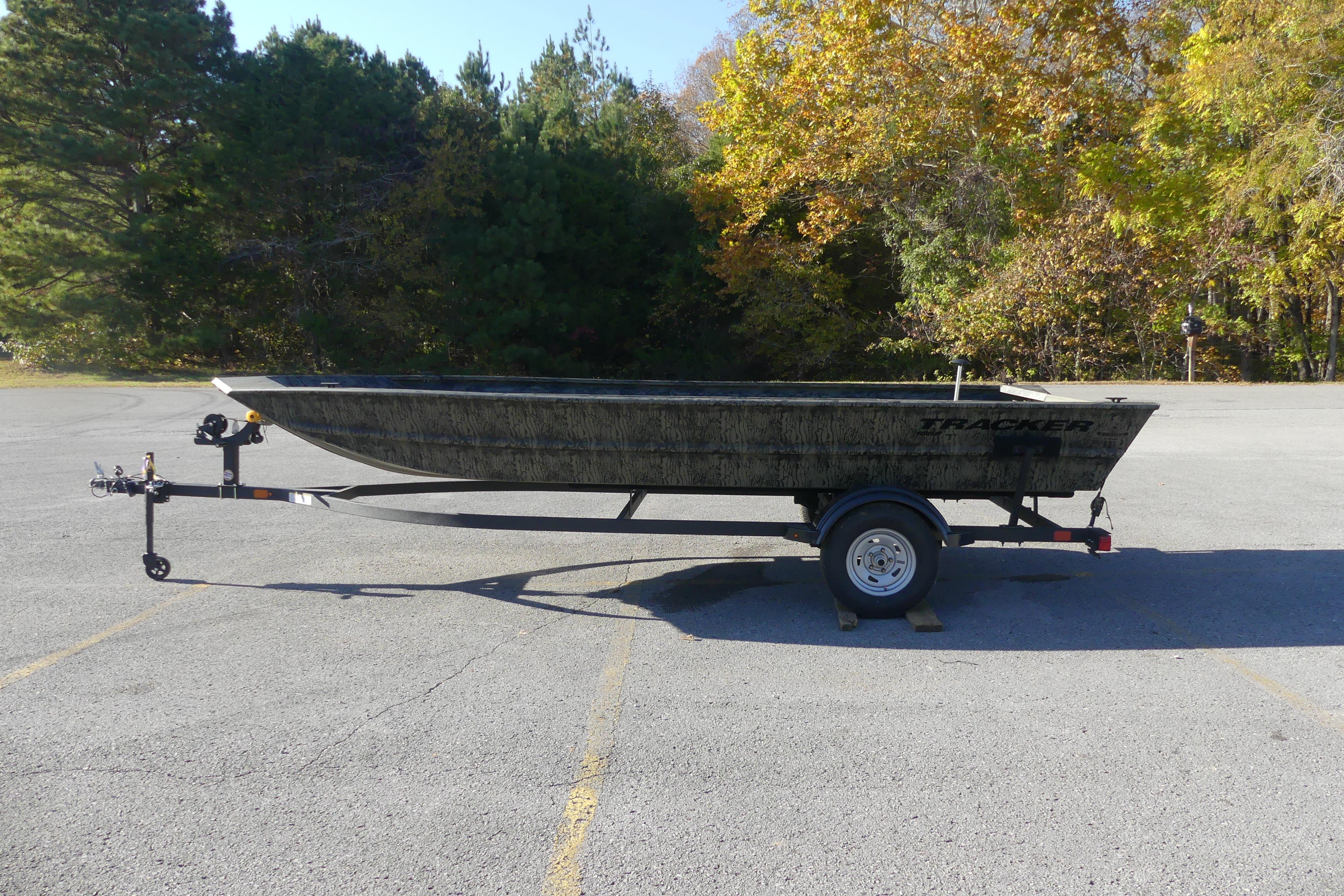 2026 Tracker Grizzly 1860 Utility boat on trailer in parking lot, surrounded by trees.