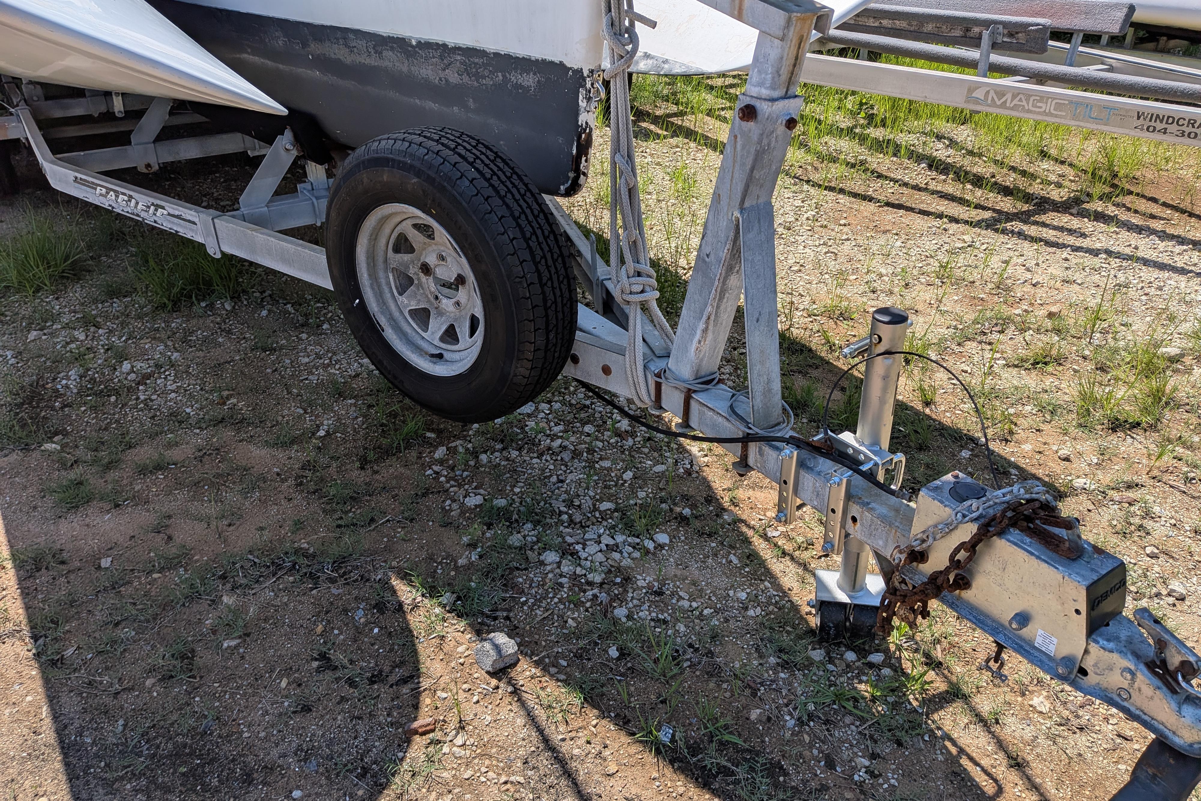 Trailer for 1991 Corsair F-27 sailboat on gravel surface, featuring sturdy metal frame and wheel.