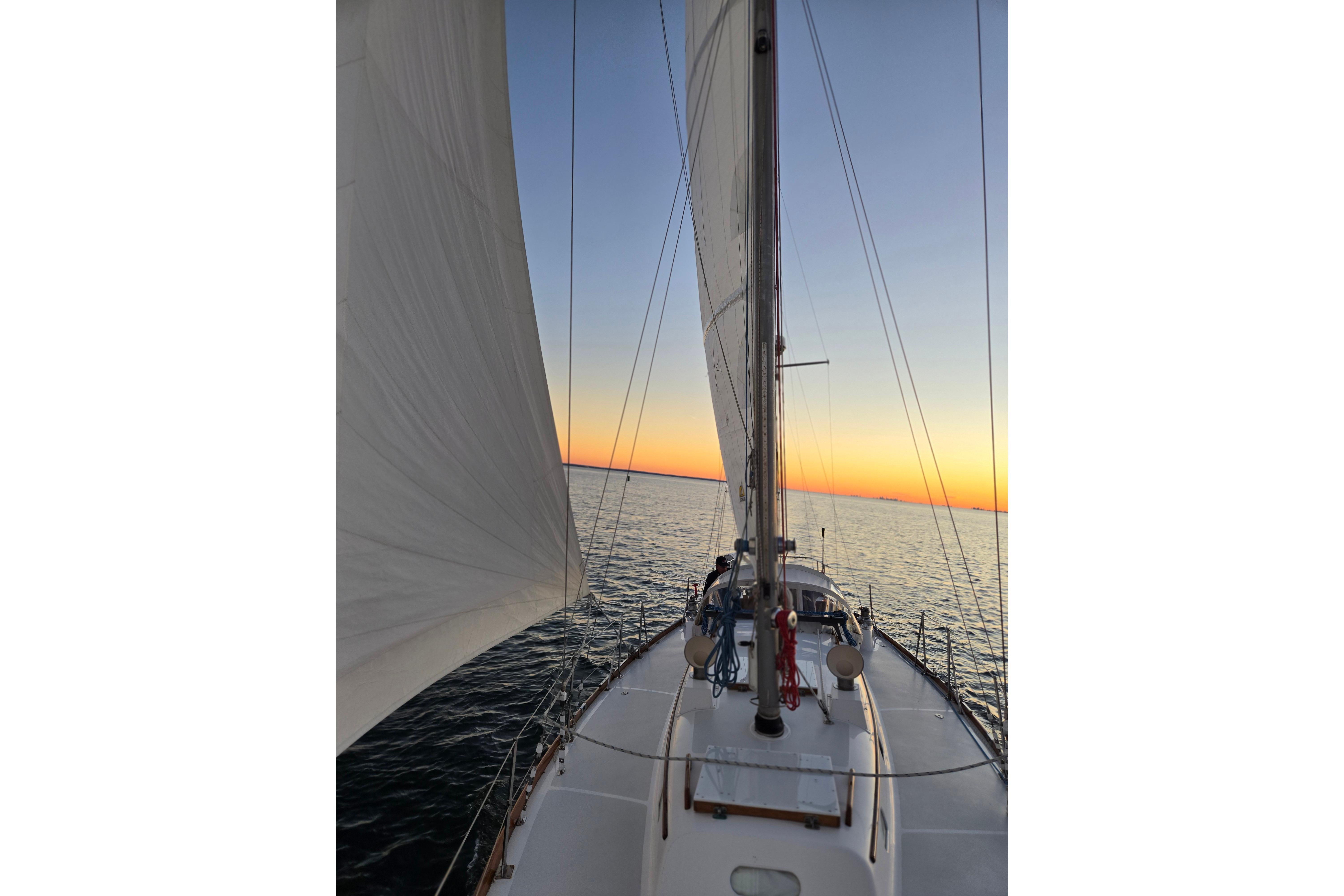 Sailing on a 1970 Hinckley Bermuda 40 at sunset, calm sea and vibrant sky.