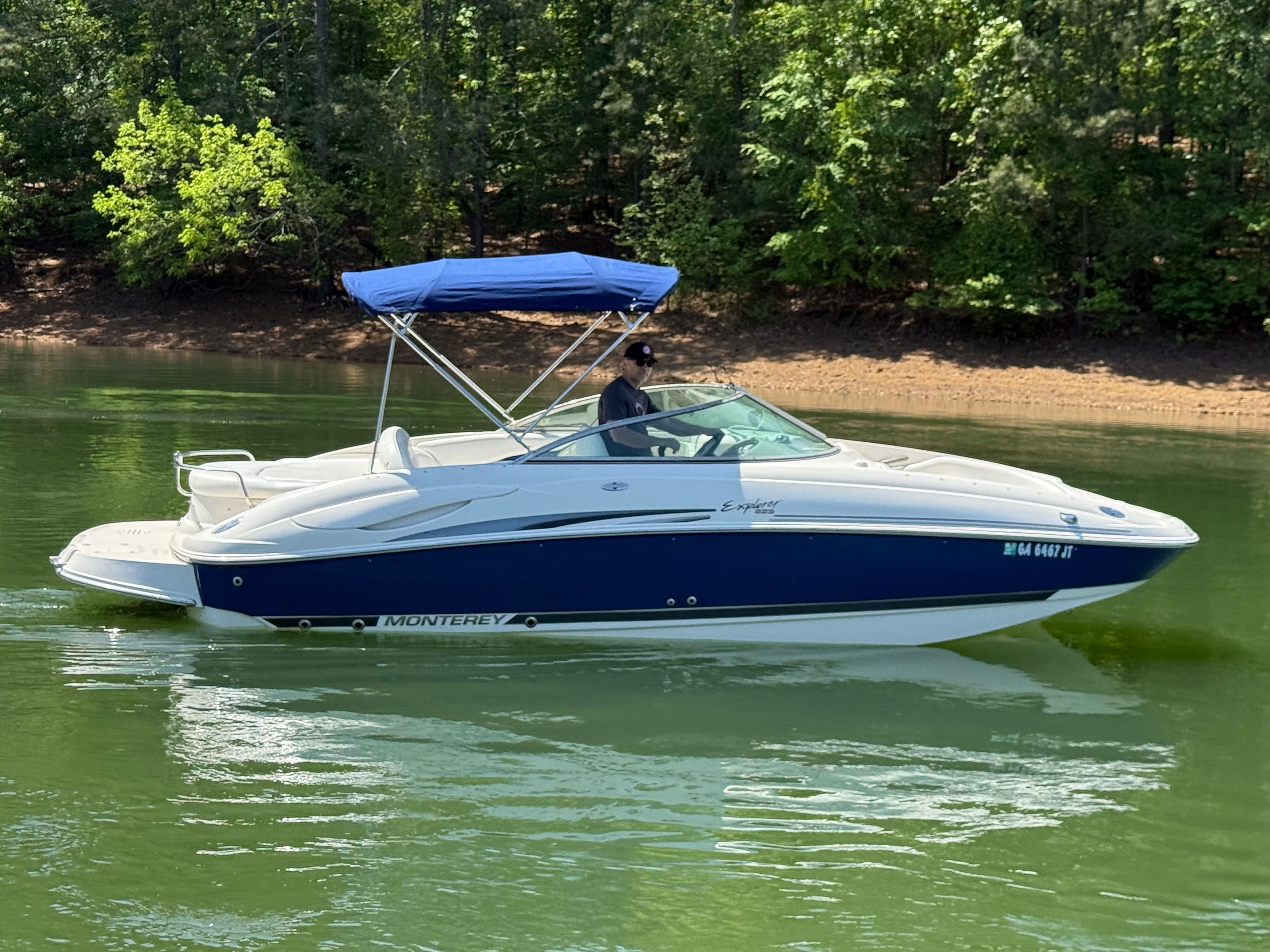A white and blue 2005 Monterey 223 Explorer Sport boat with a sunshade on a calm lake.