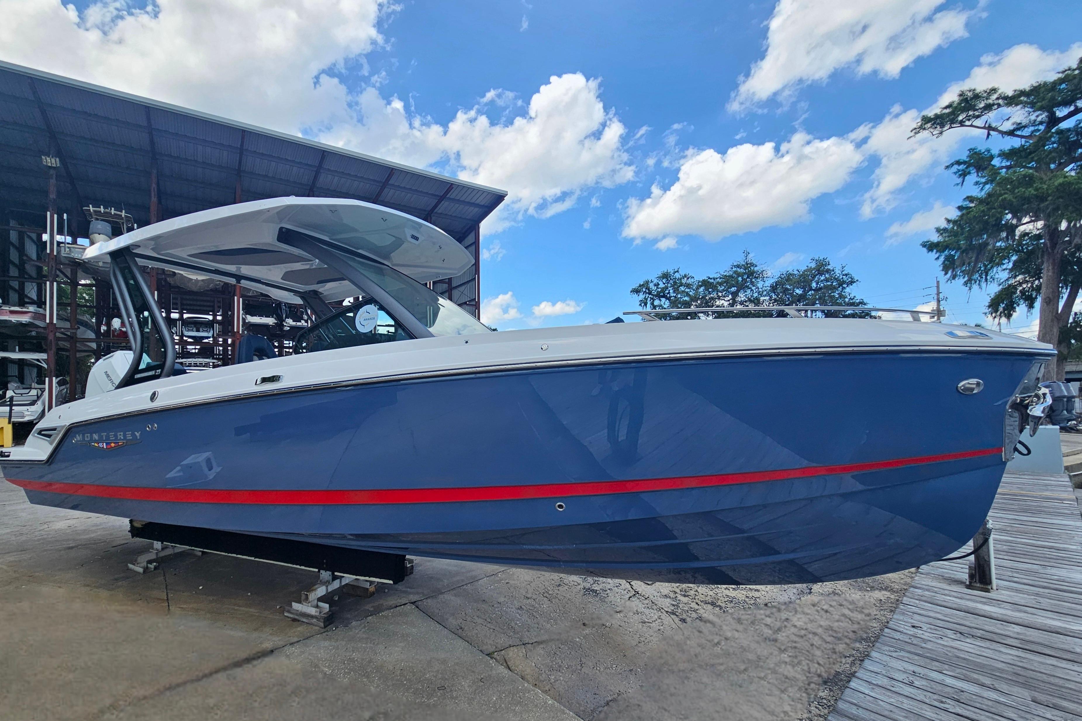 2026 Monterey Elite 27 OB boat with blue hull and red stripe, docked under a clear sky.