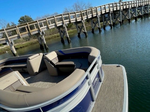 A Bennington 23SXSRC pontoon boat on calm water, with a wooden bridge in the background.