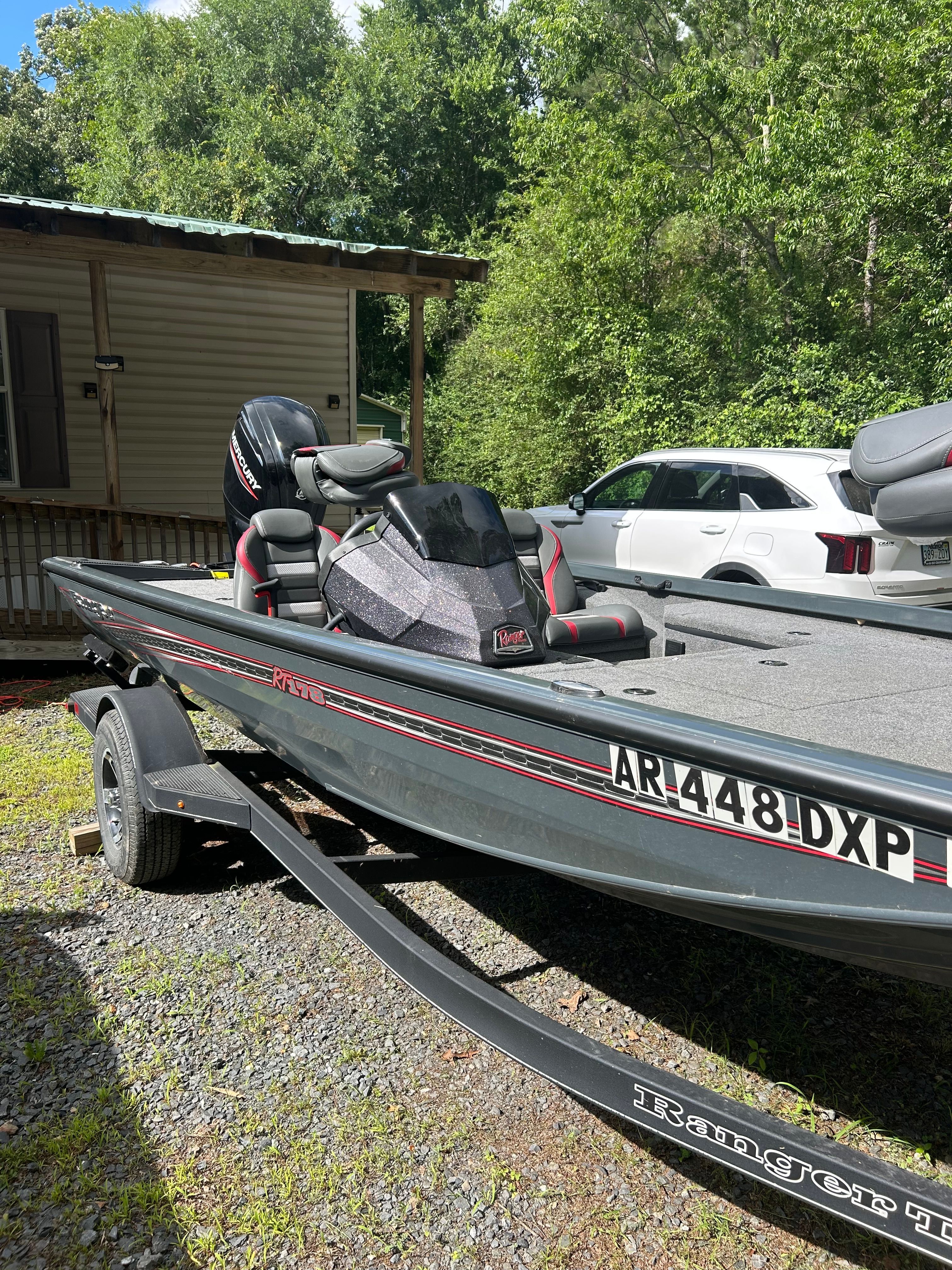 A Ranger RT178 boat on a trailer, parked beside a house in a green area.