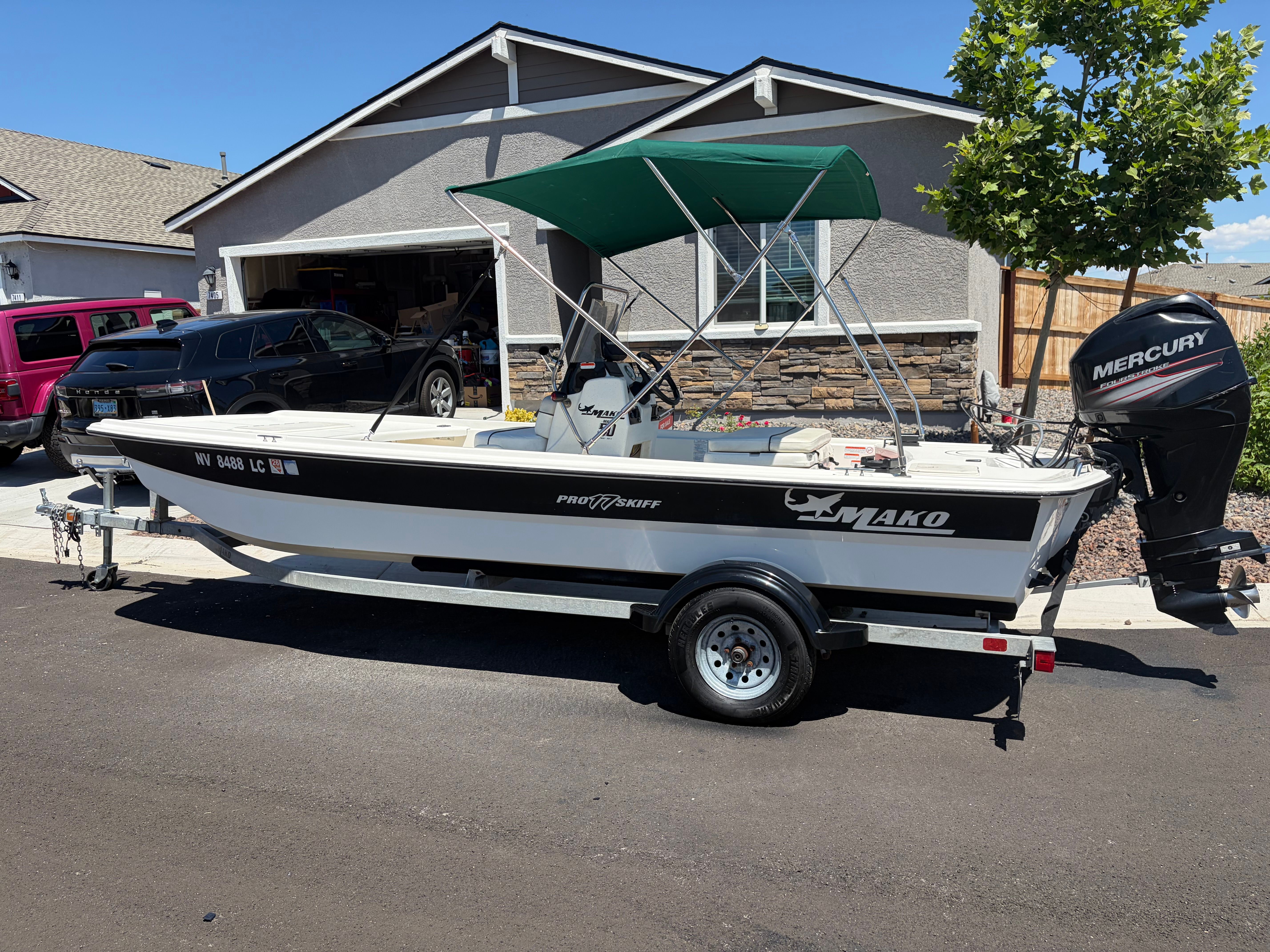 A 2017 Mako Pro Skiff 17 CC with a green canopy, parked on a trailer in front of a house.