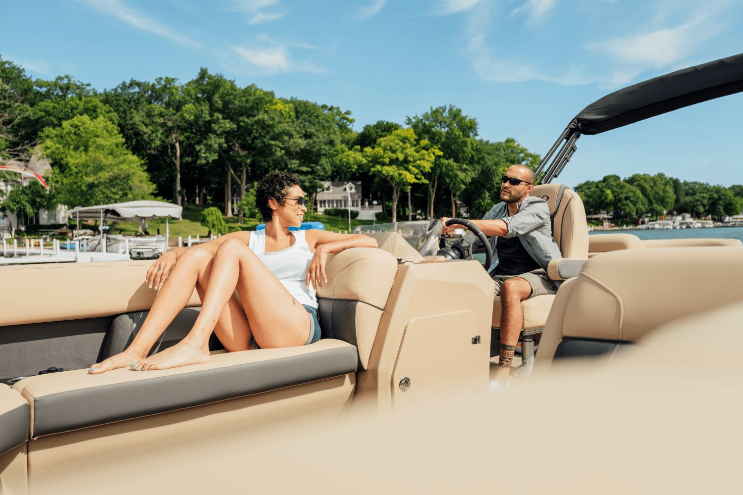 Two people relax on a Harris Cruiser 230 pontoon boat on a lake.