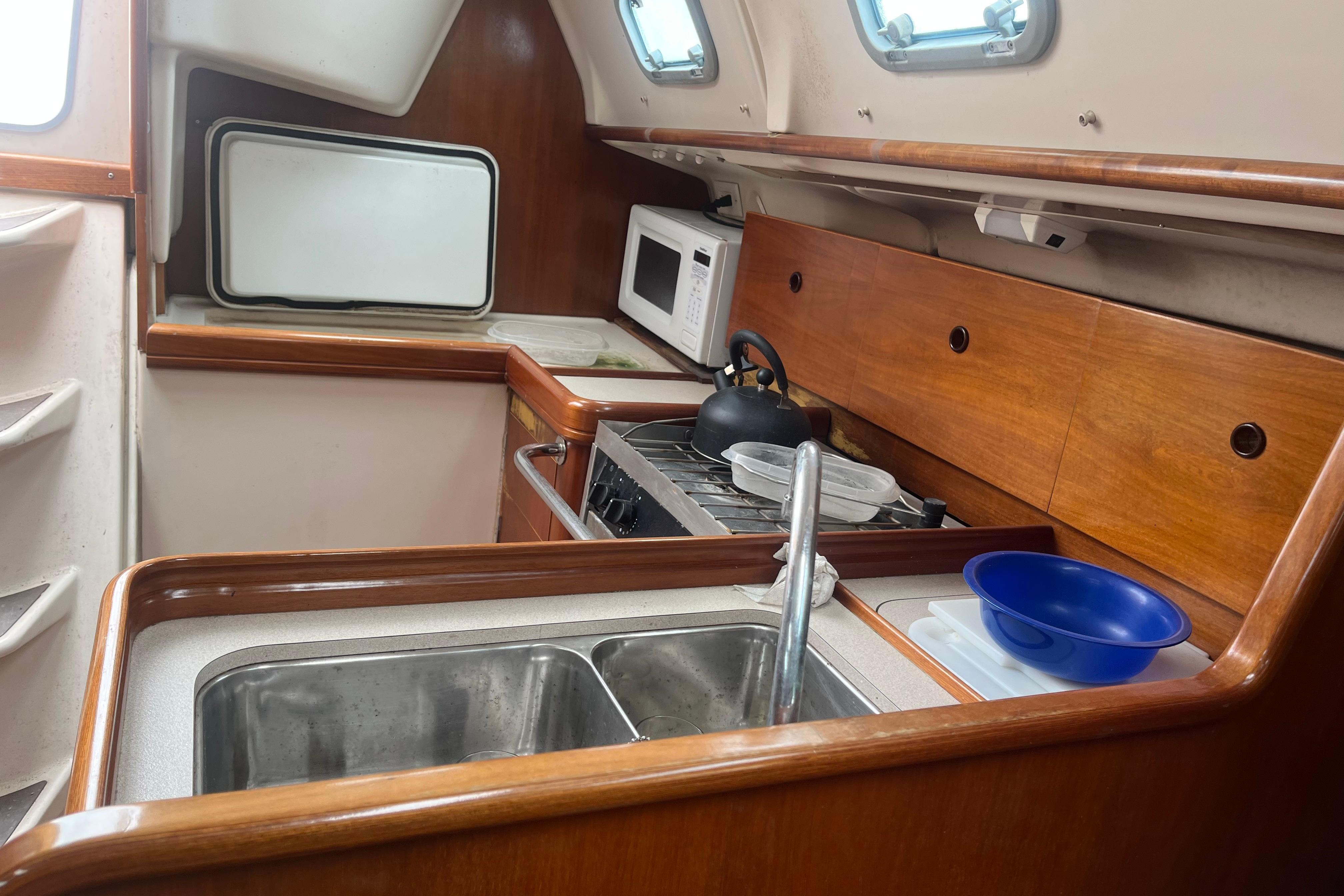 Interior of 1999 Benneteau 321 Oceanis yacht kitchen with sink, stove, and microwave.