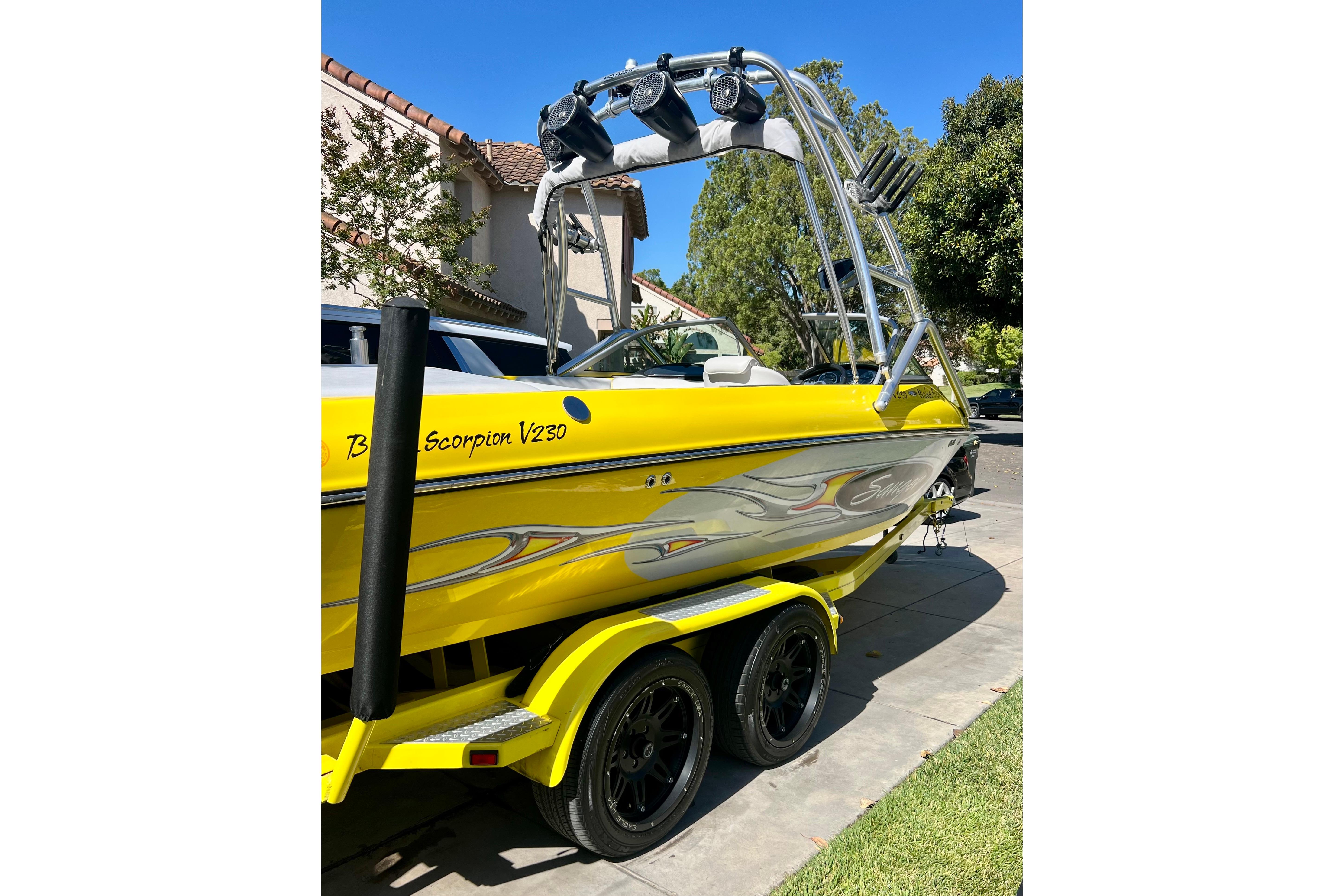 Yellow 2006 Sanger V230 boat with custom graphics on a trailer, parked in a driveway.