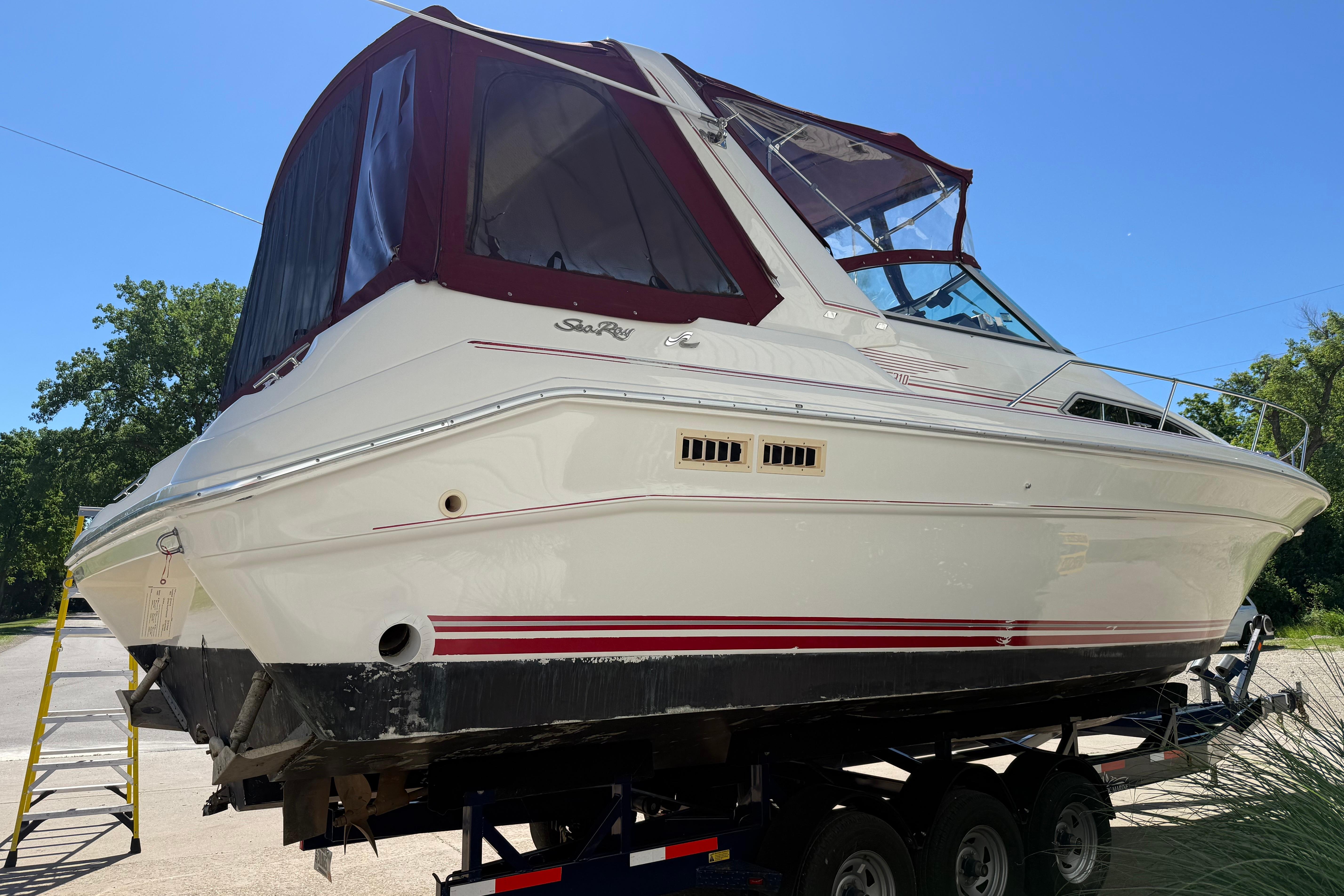 1990 Sea Ray 310 Express Cruiser on trailer, featuring maroon canopy and sleek white hull.