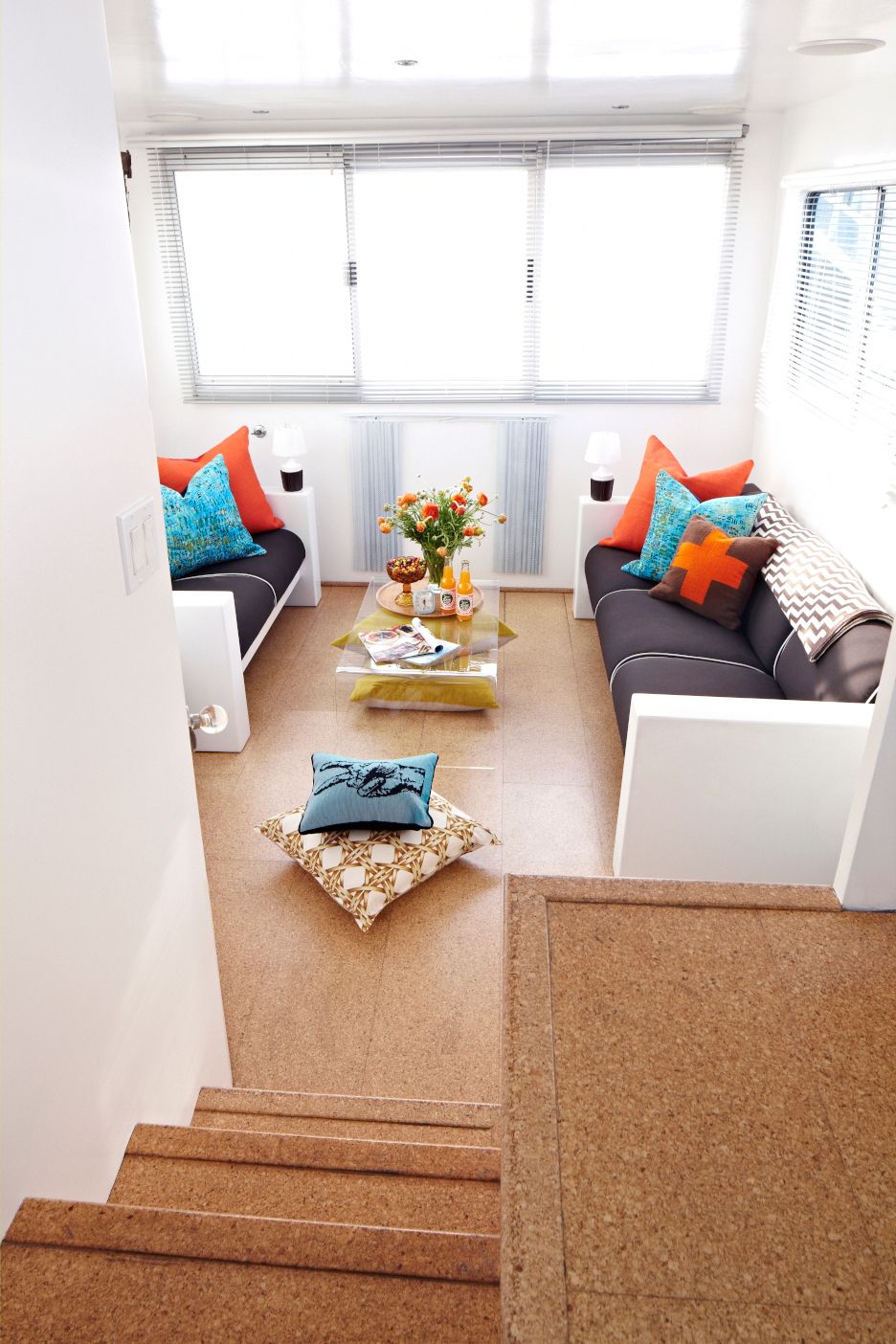 Interior of a houseboat with modern sofas, colorful cushions, and a table with flowers.