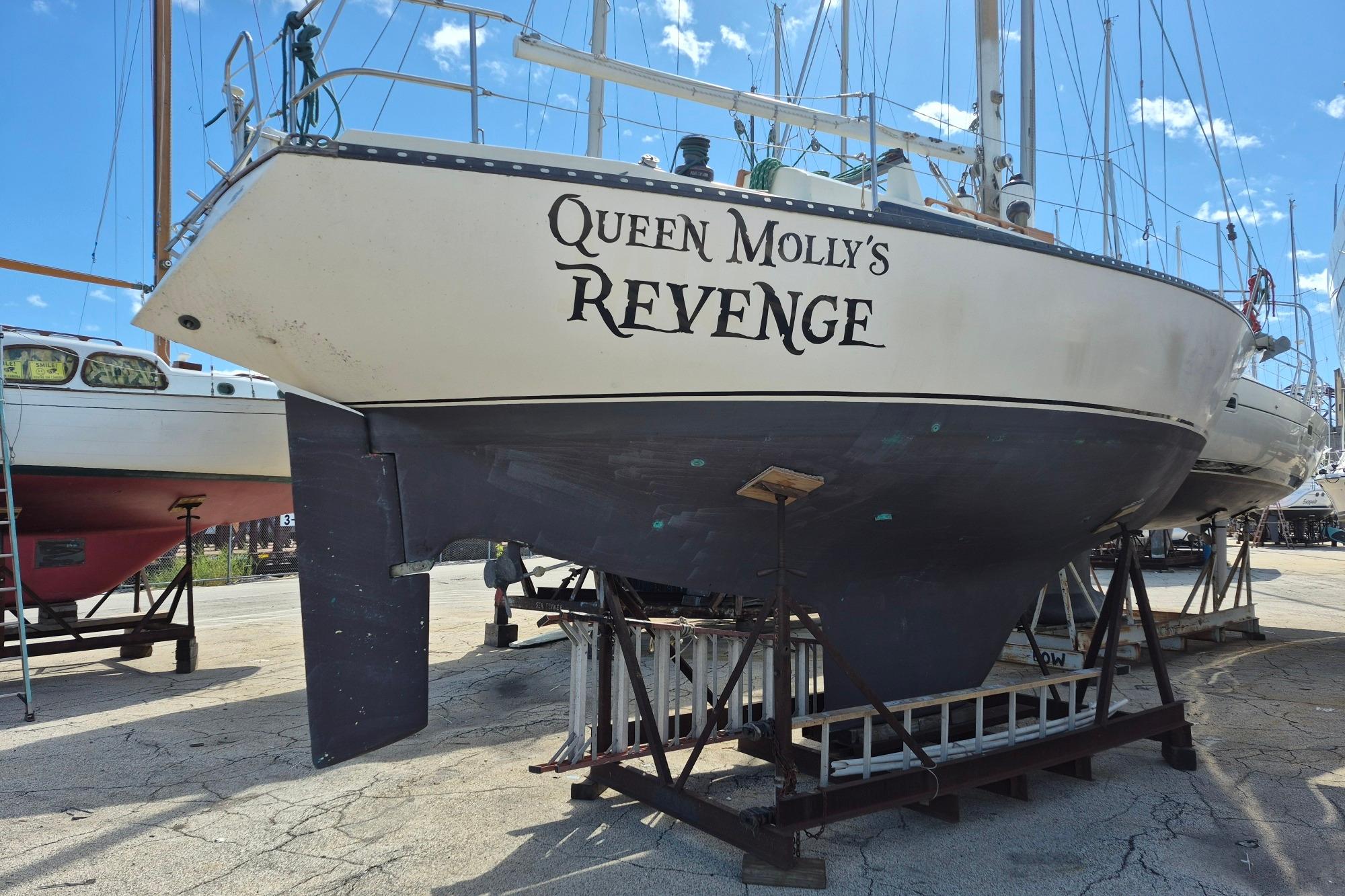 1978 Kettenburg 32 sailboat "Queen Molly's Revenge" on dry dock, blue sky background.