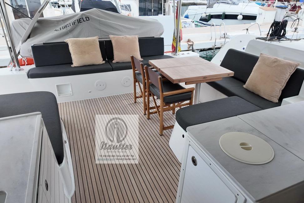 Outdoor seating area on 2023 Lagoon 46 yacht with cushions and wooden table.