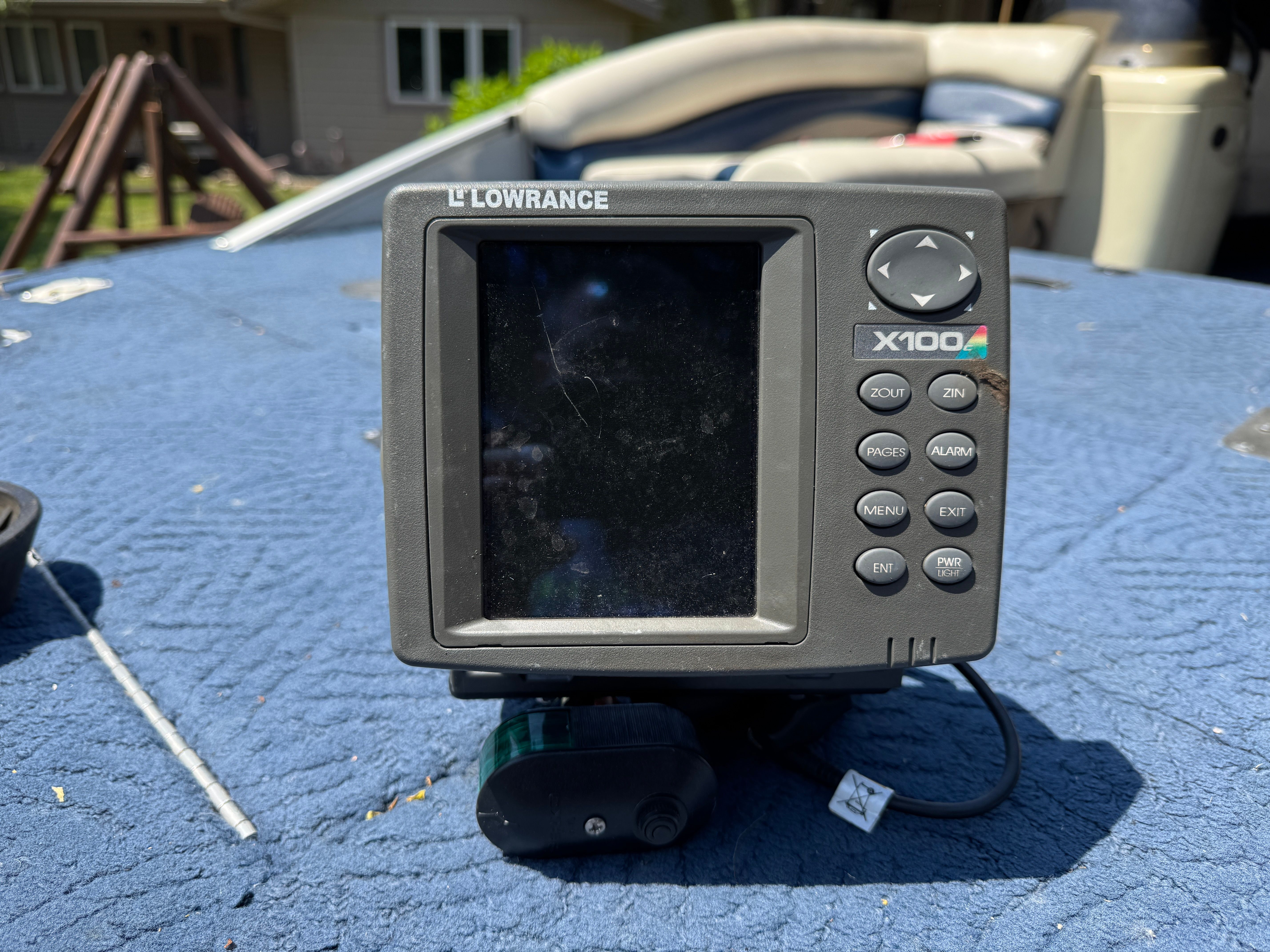 A fish finder on a blue boat carpet, with a house in the background.