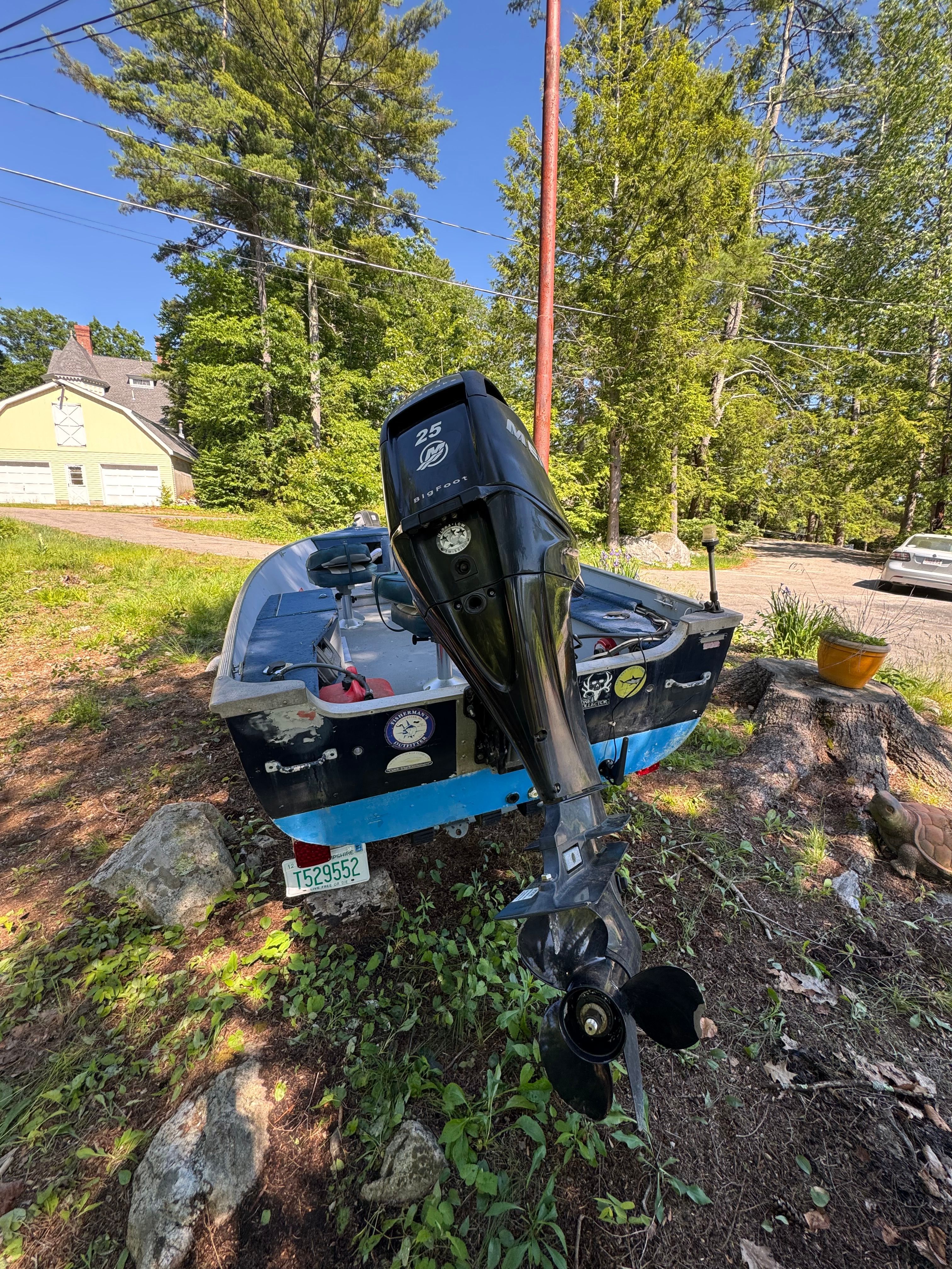 A blue boat with an outboard motor is on a grassy area.