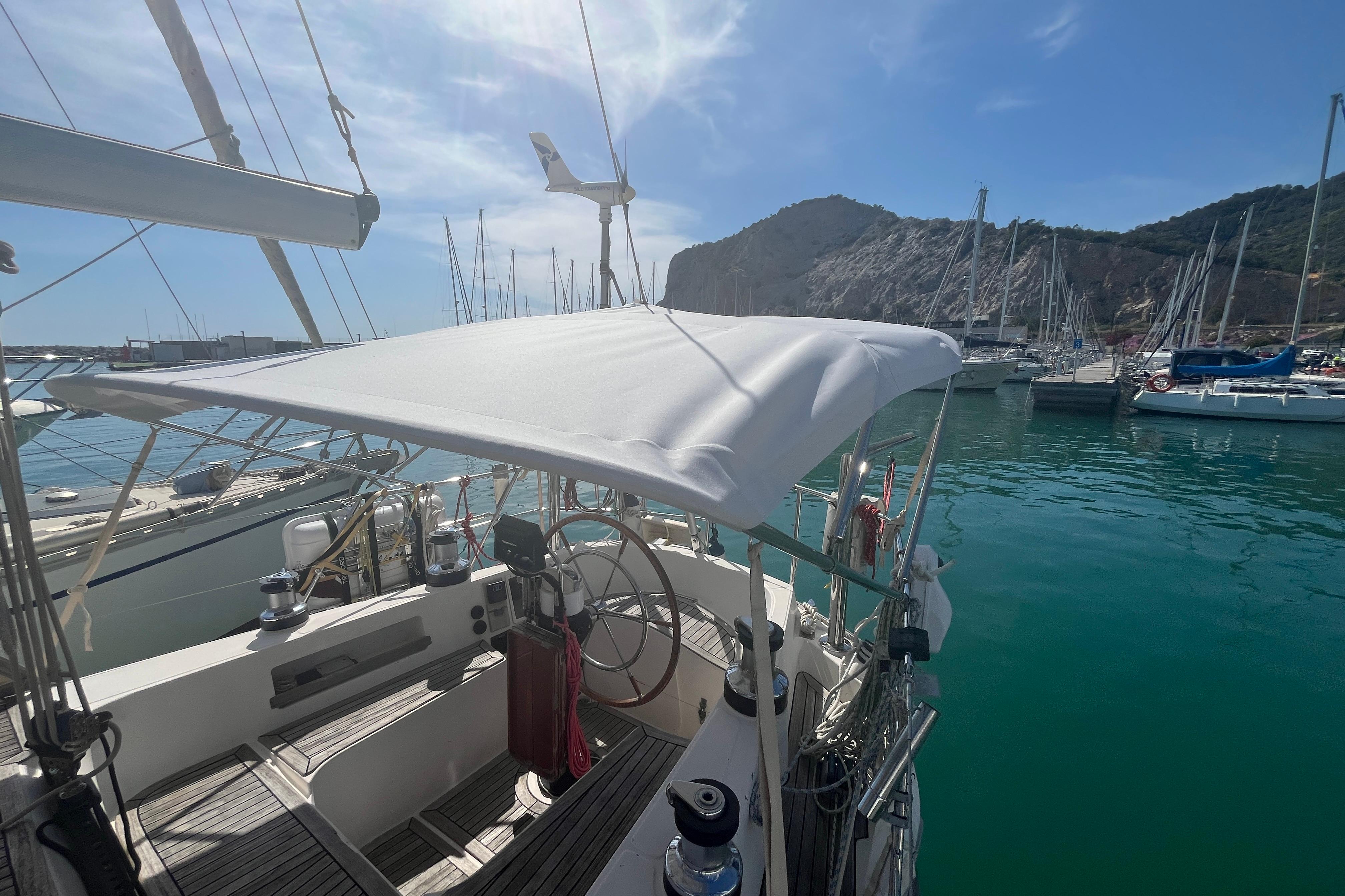 Sailboat Belliure 41, 1995 model, docked in a sunny marina with scenic mountain backdrop.