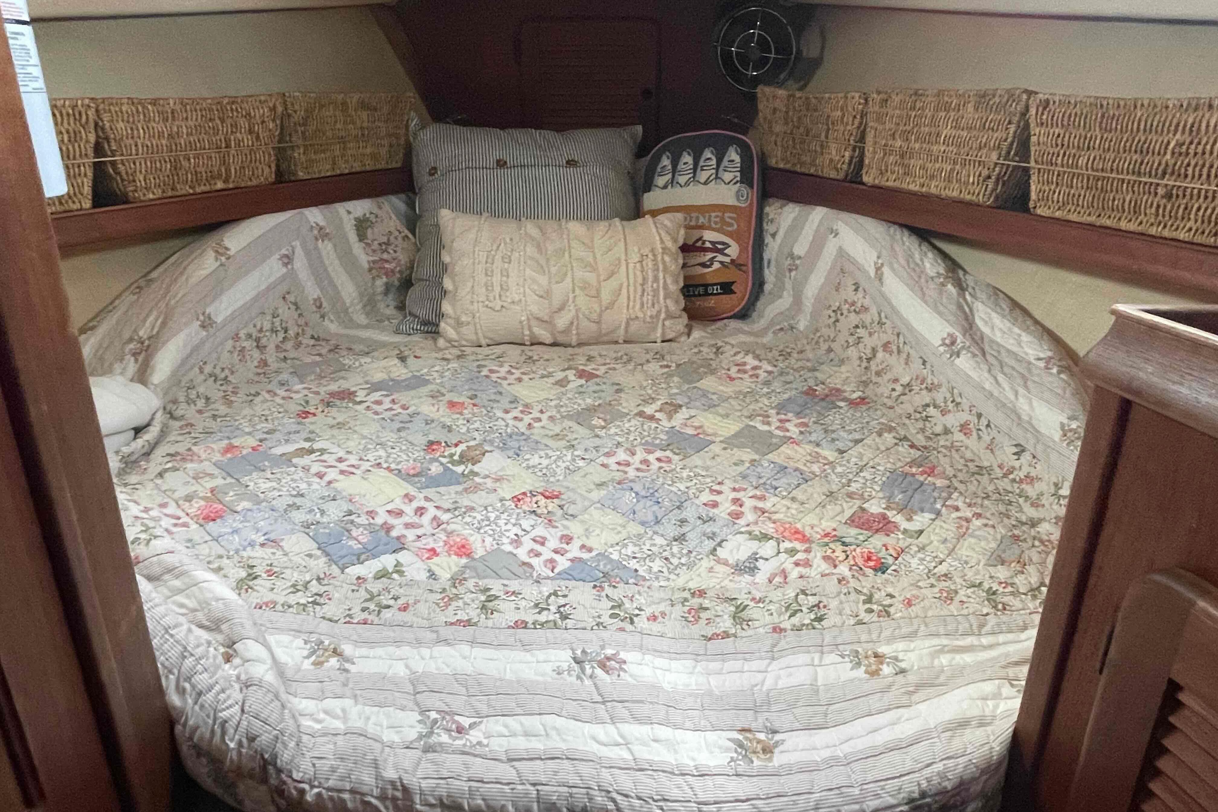 Cozy cabin interior of 1989 Island Packet 35 sailboat with floral quilt and wicker storage.