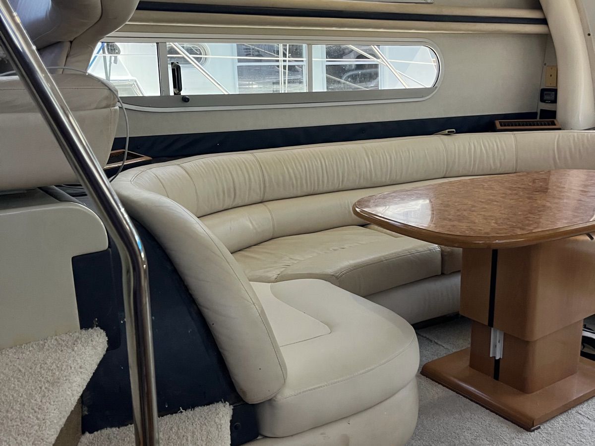 Interior of a 1999 Sealine F44 with cream leather seating and a wooden table.