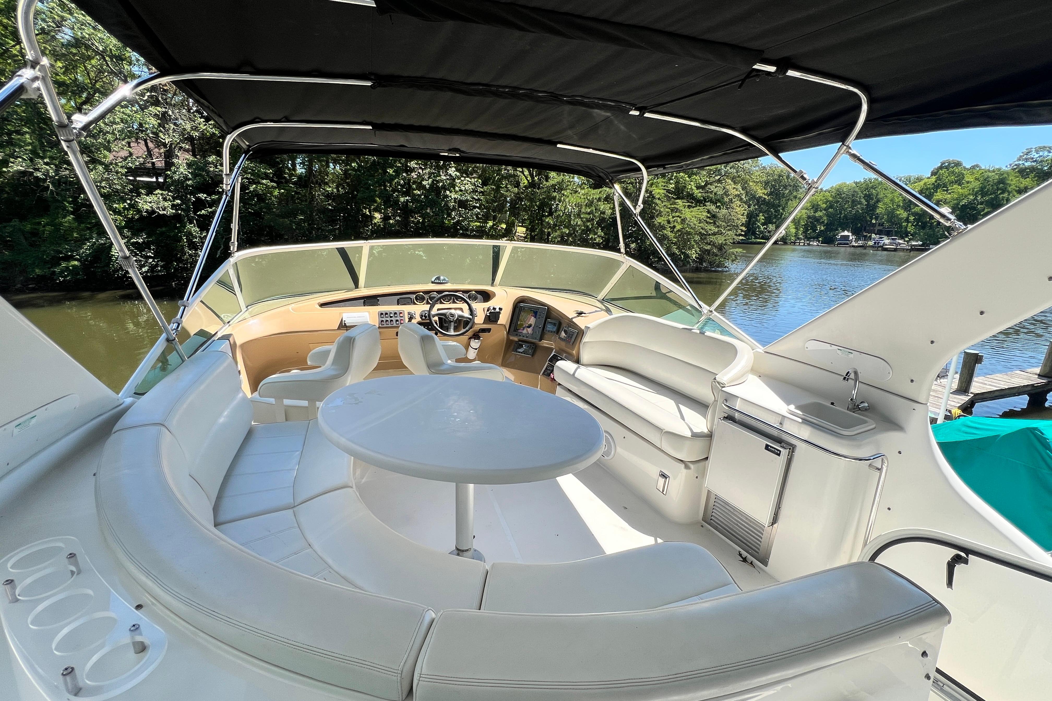 2003 Carver 450 Voyager Pilothouse interior with seating, table, and helm, docked by a scenic river.