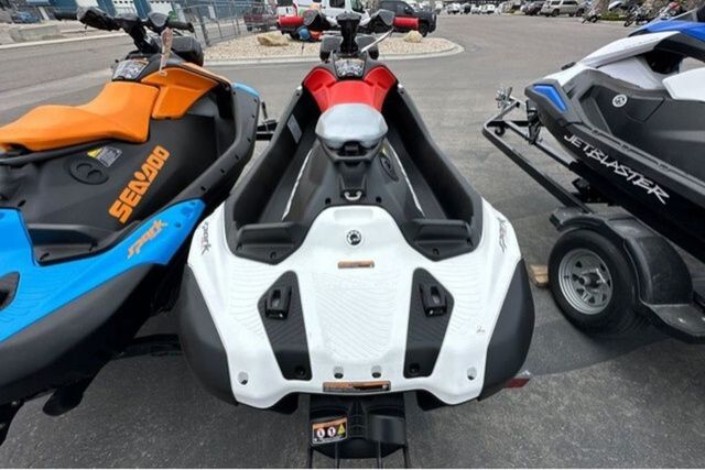 Three jet skis are parked on a lot. The middle one is a Sea-Doo SPARK TRIXX 90.