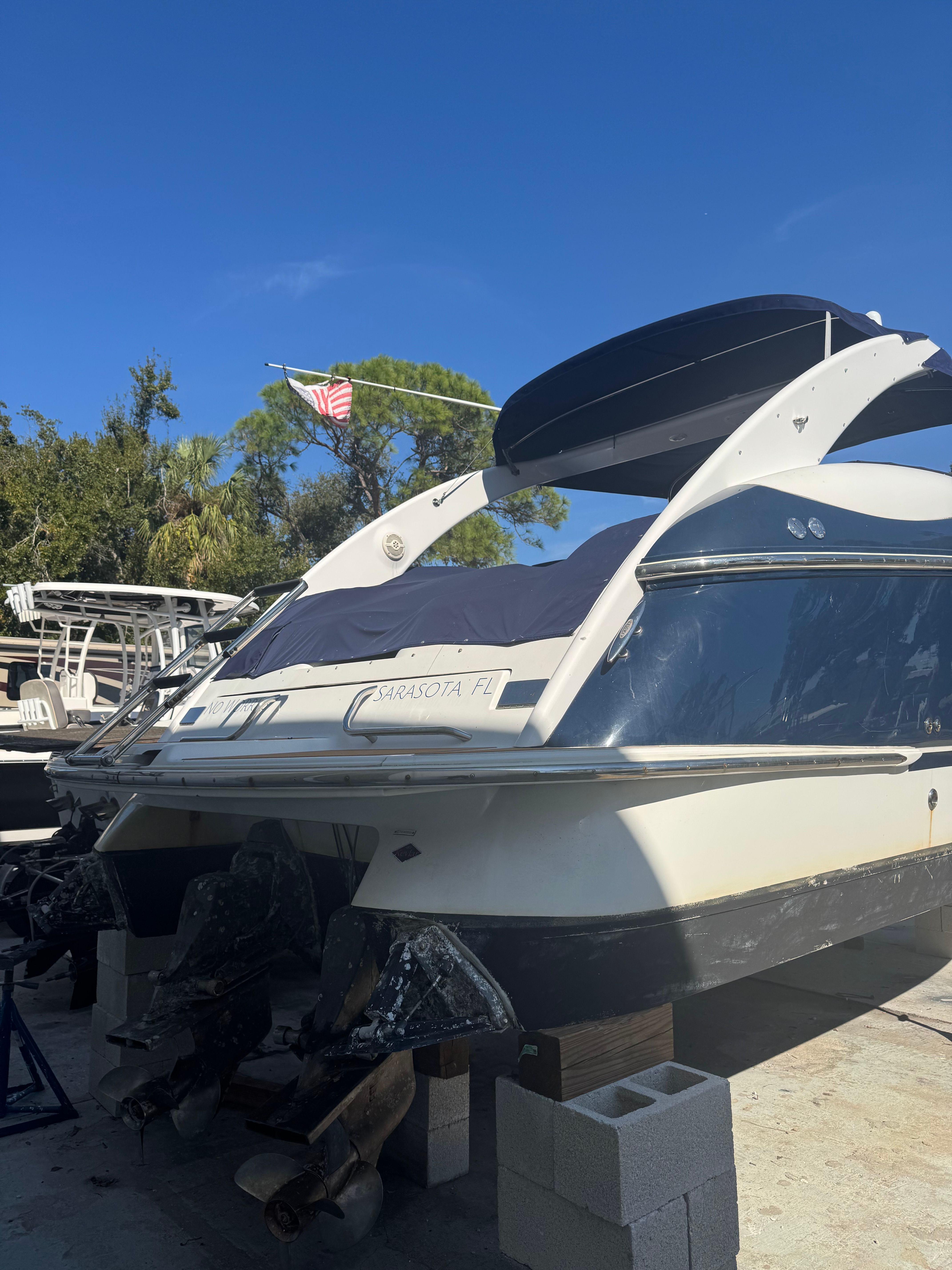 A 2003 Cobalt 360 boat is on blocks. It features twin outboard engines and a cover.