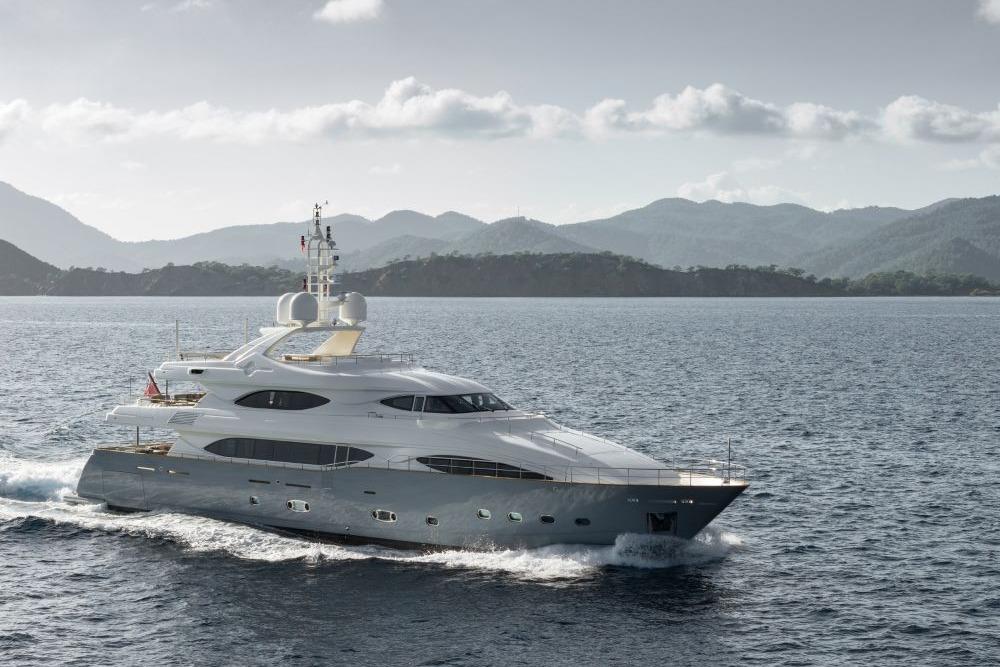 Luxurious 2009 CRN 129 yacht cruising on serene waters with scenic mountain backdrop.