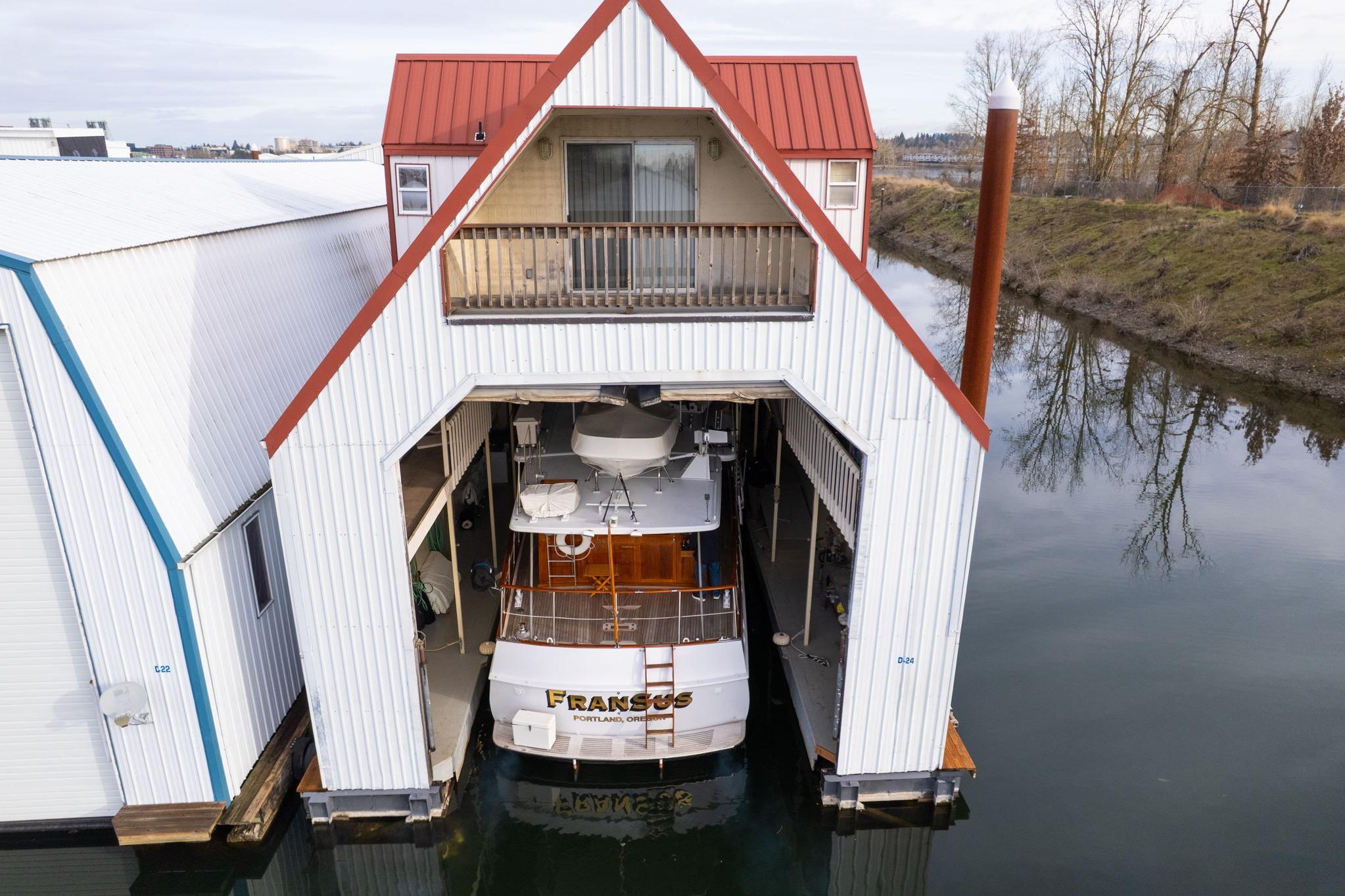Custom 1976 boathouse with docked boat, featuring red roof and balcony, on calm water.