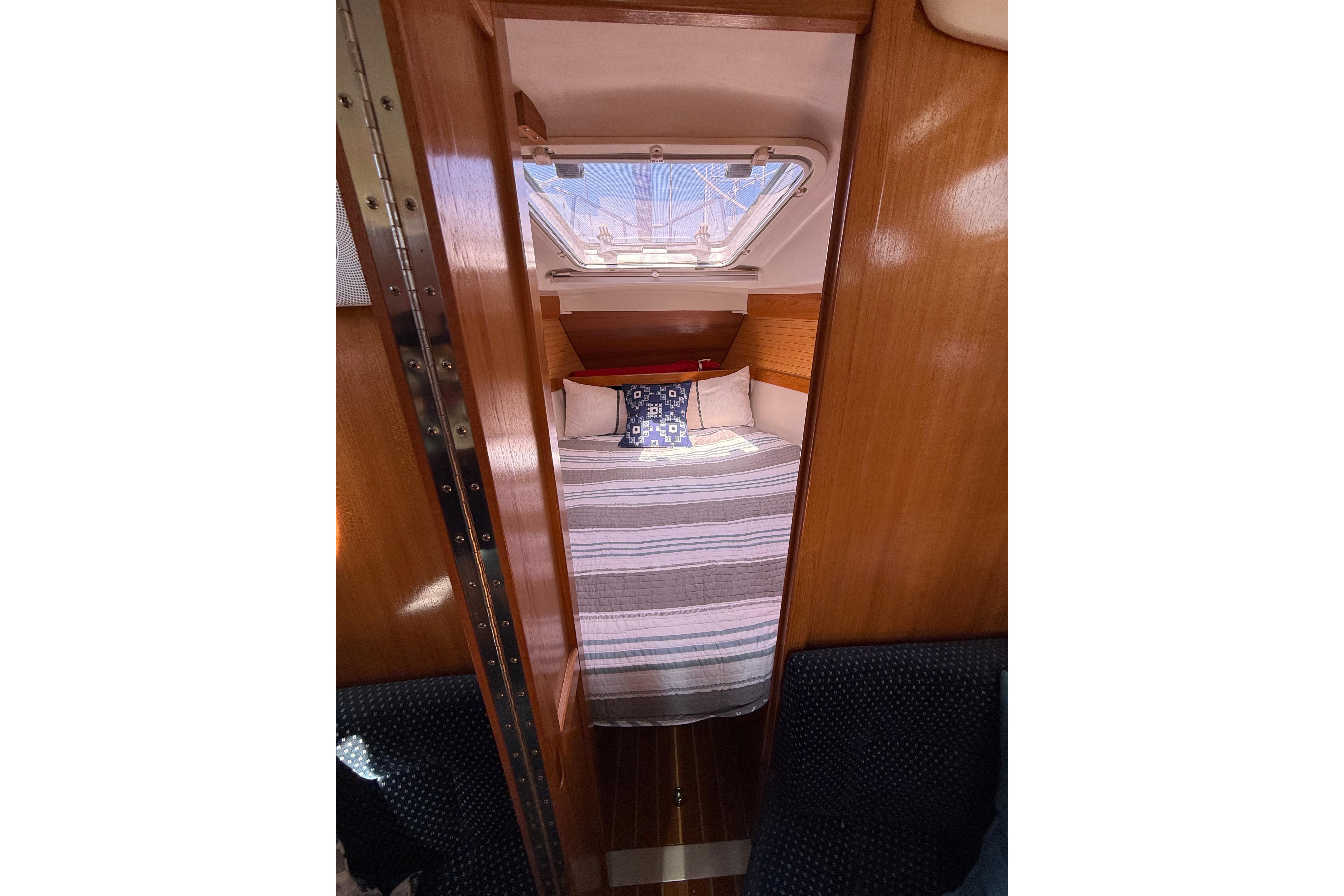 Cozy cabin interior of a 2004 Catalina 320 sailboat with striped bedding and wooden finish.