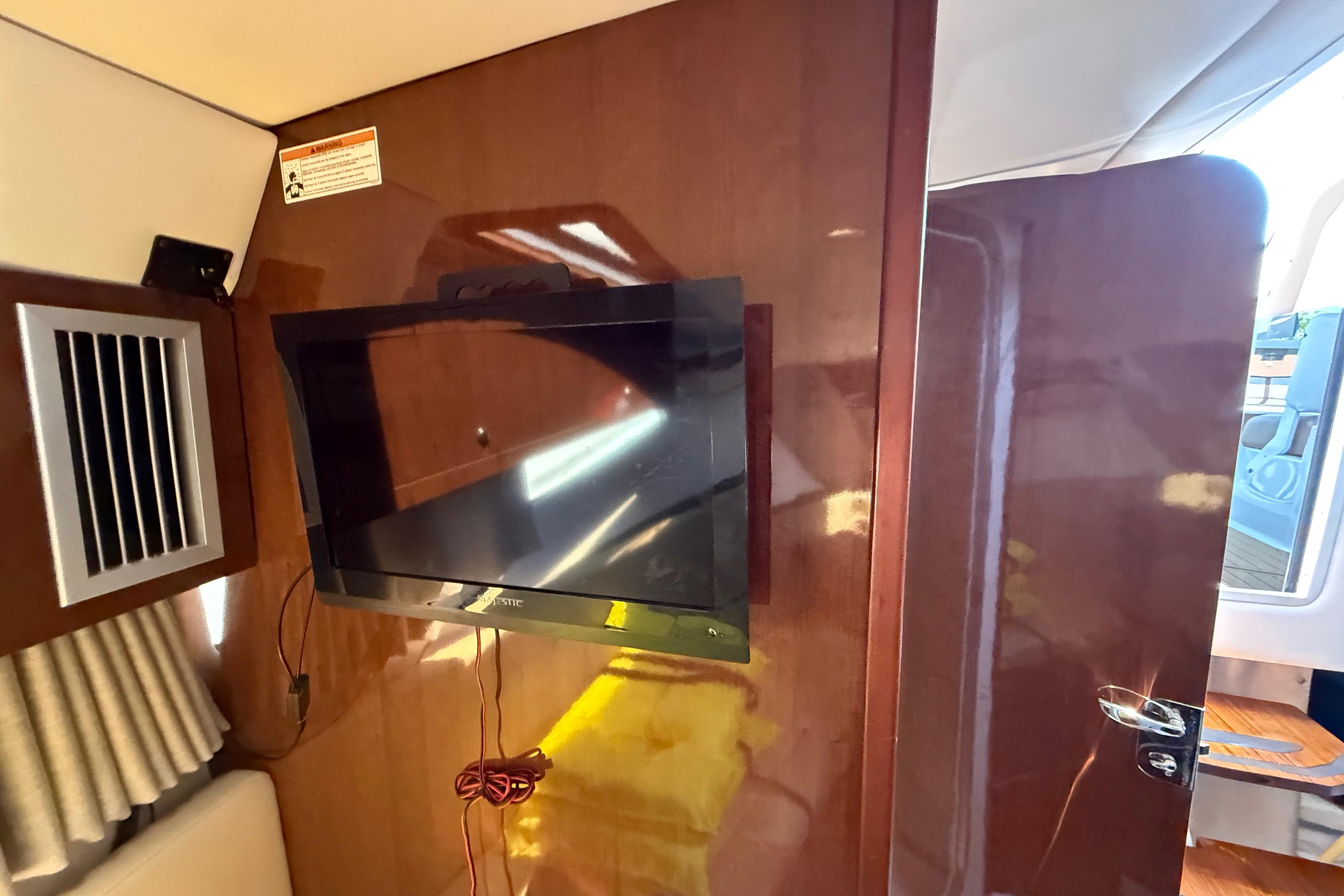 Interior of 2017 Four Winns V275 boat featuring a mounted TV and wooden paneling.