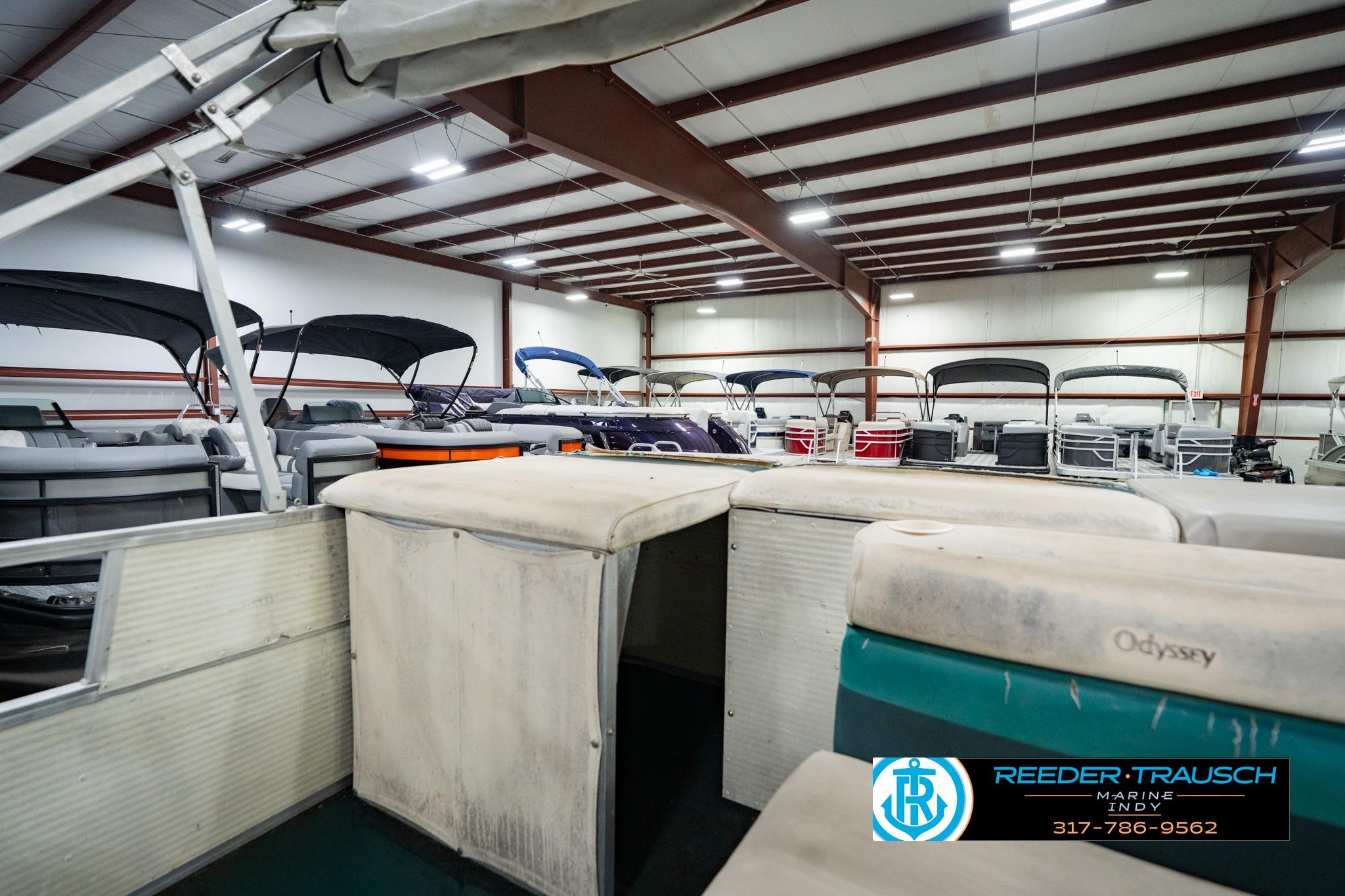 Indoor showroom displaying a 1998 Odyssey 25 boat with multiple pontoon boats in the background.