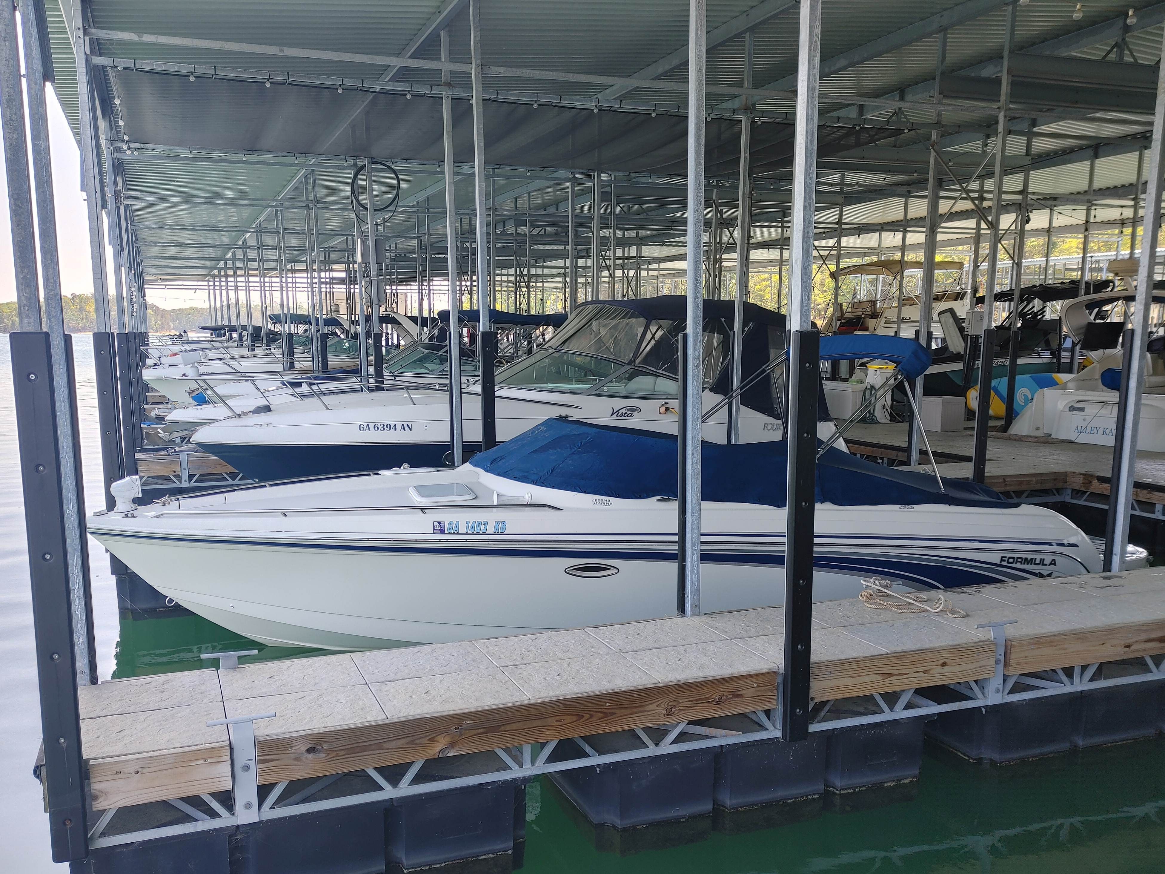 A white motorboat with a blue cover is docked in a covered marina.
