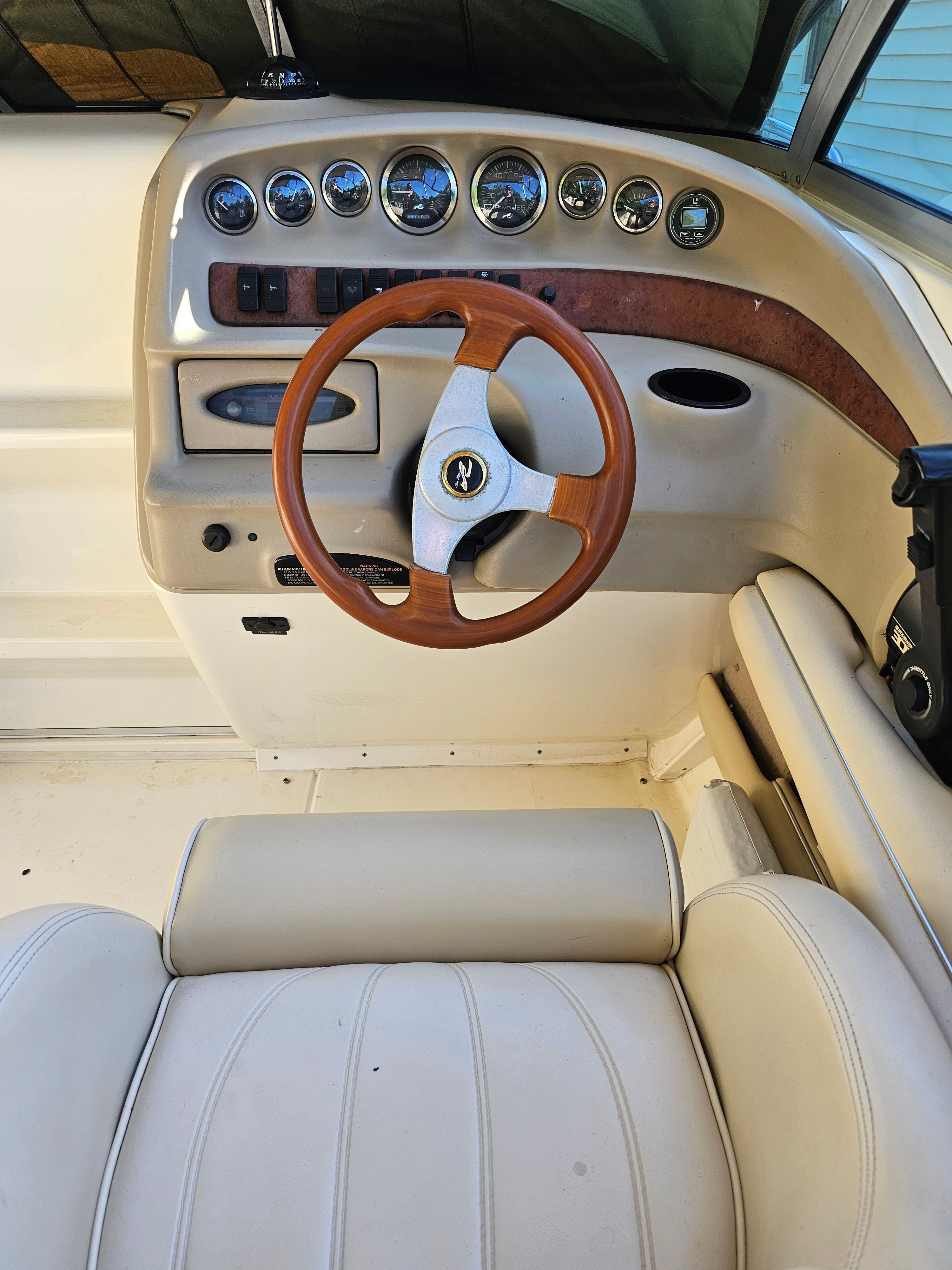 Interior view of a boat with a wooden steering wheel and cream-colored seats.