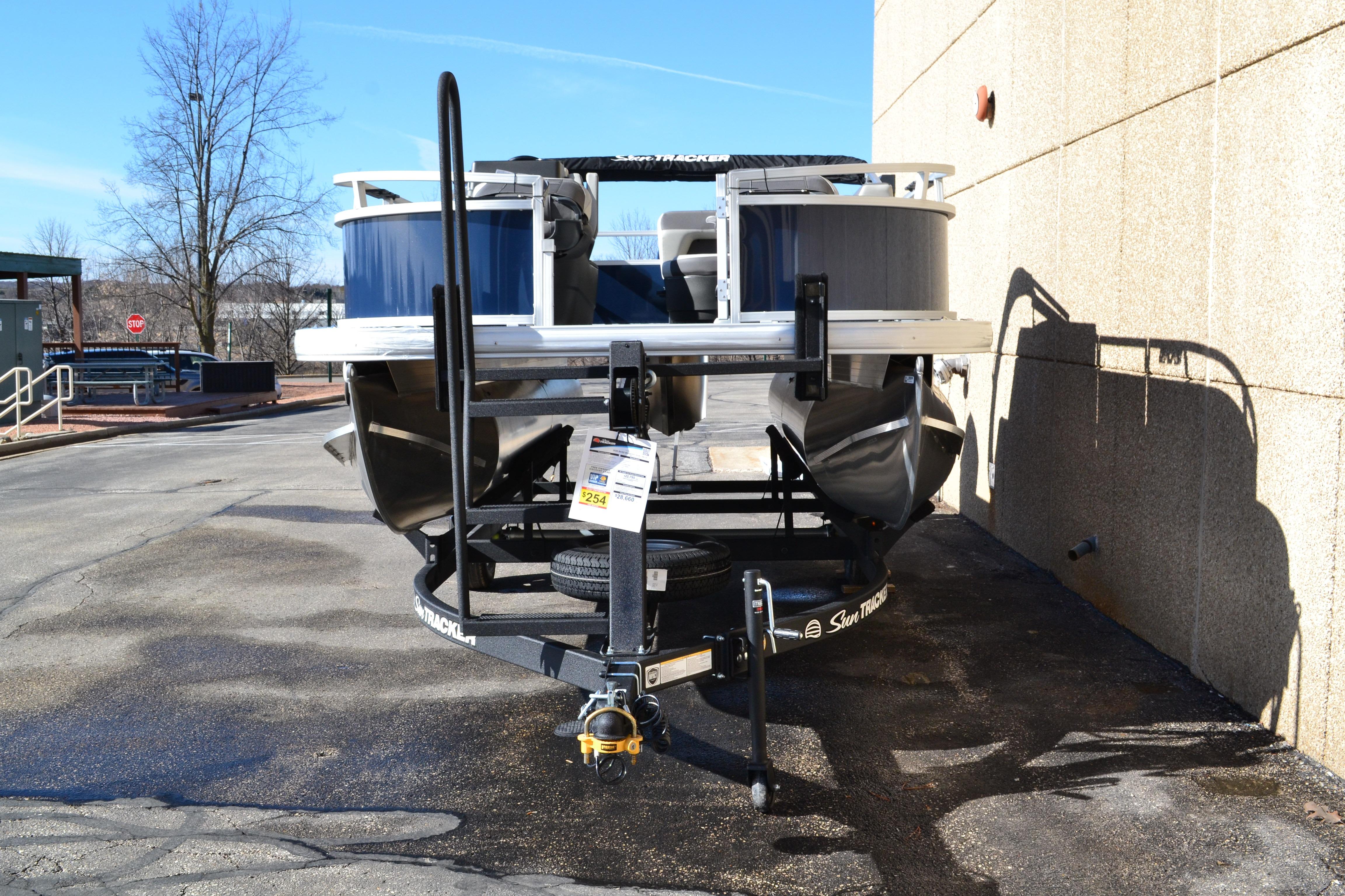 2026 Sun Tracker Bass Buggy 16 XL Select pontoon boat on trailer, parked outdoors.