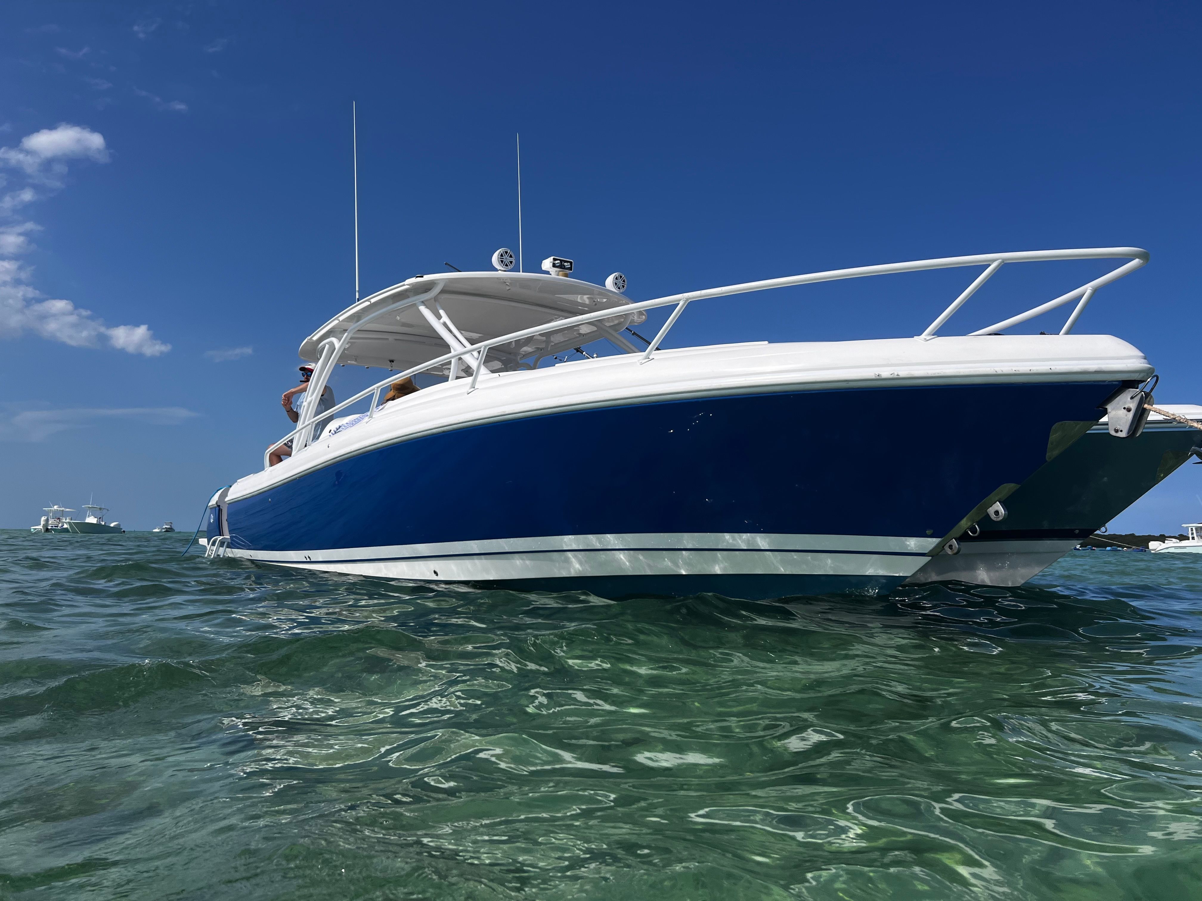 A blue and white 2014 Intrepid 375 Walkaround floats on clear water under a blue sky.