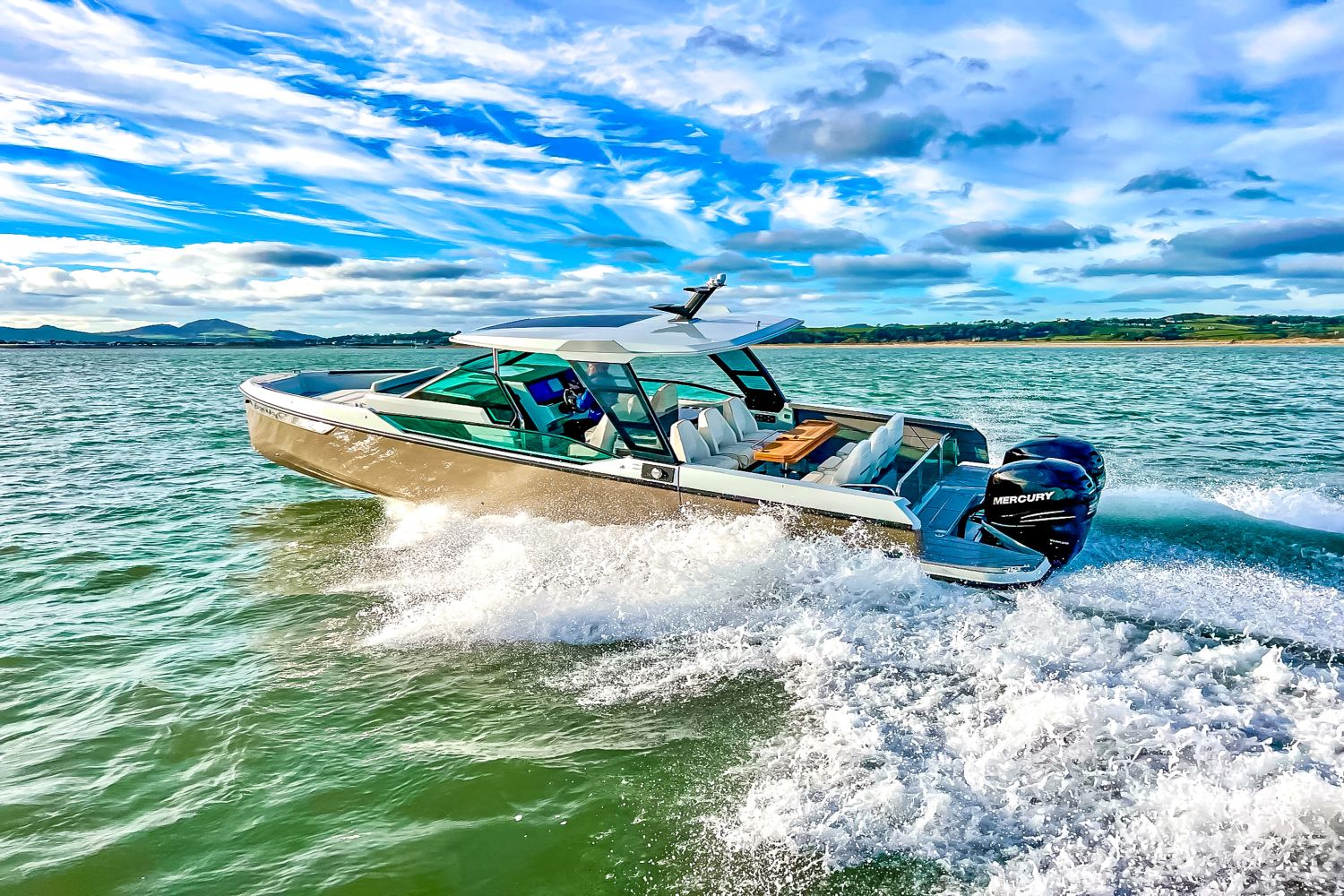 A Saxdor SX320 GTO boat speeds across the water under a blue sky.