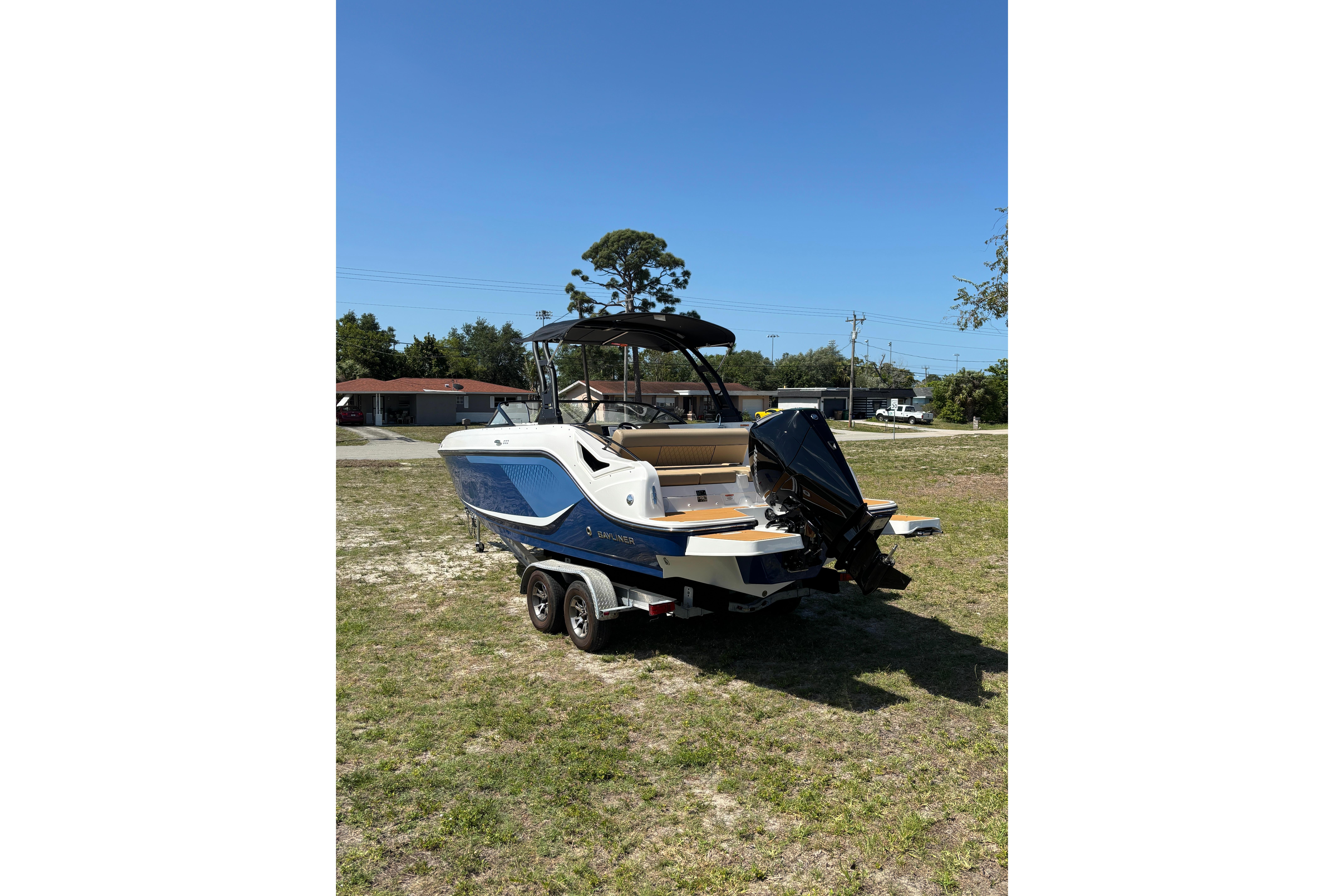 2026 Bayliner D22 boat on trailer, parked on grass under clear blue sky.