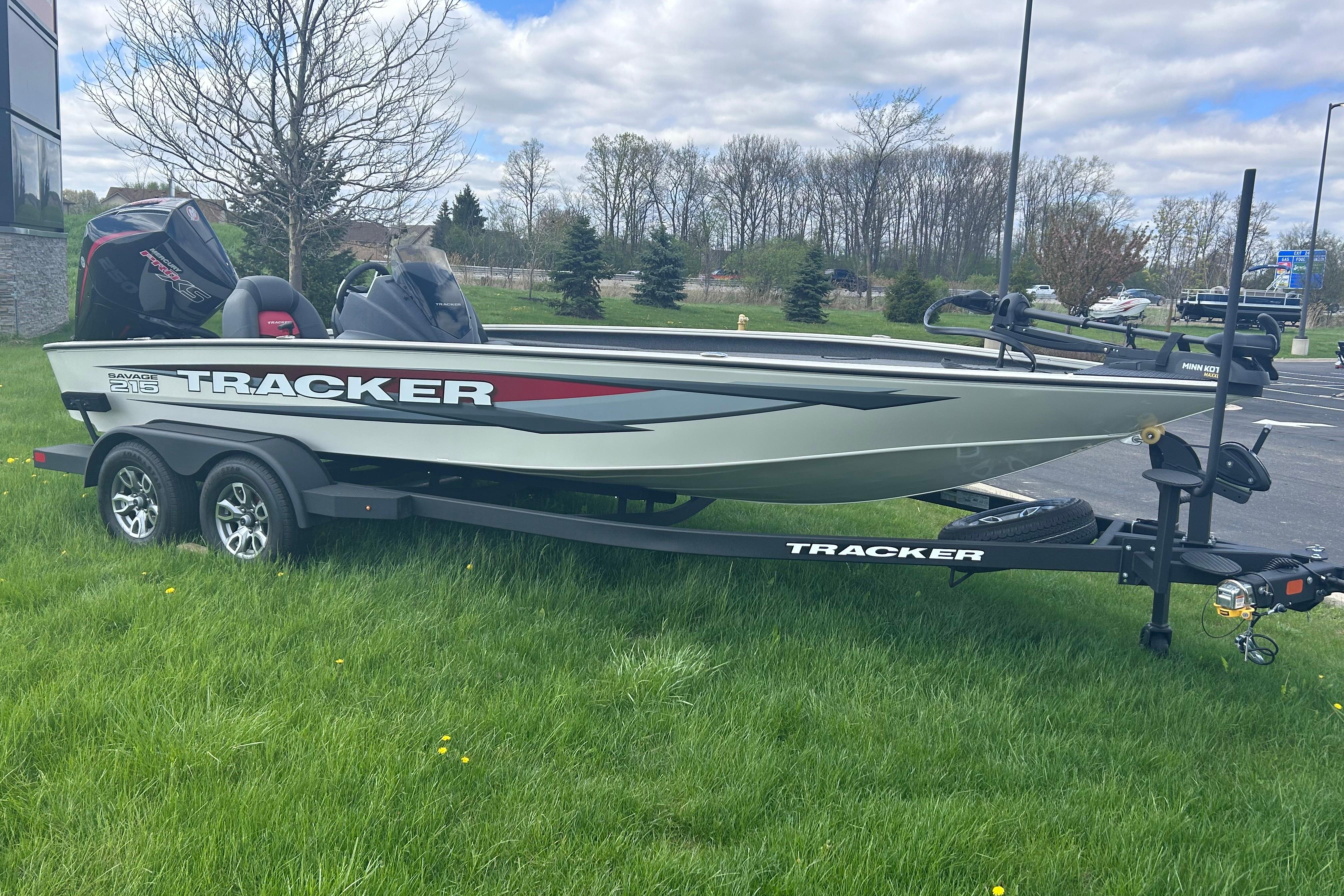 2025 Tracker Savage 215 boat on trailer, parked on grass under cloudy sky.