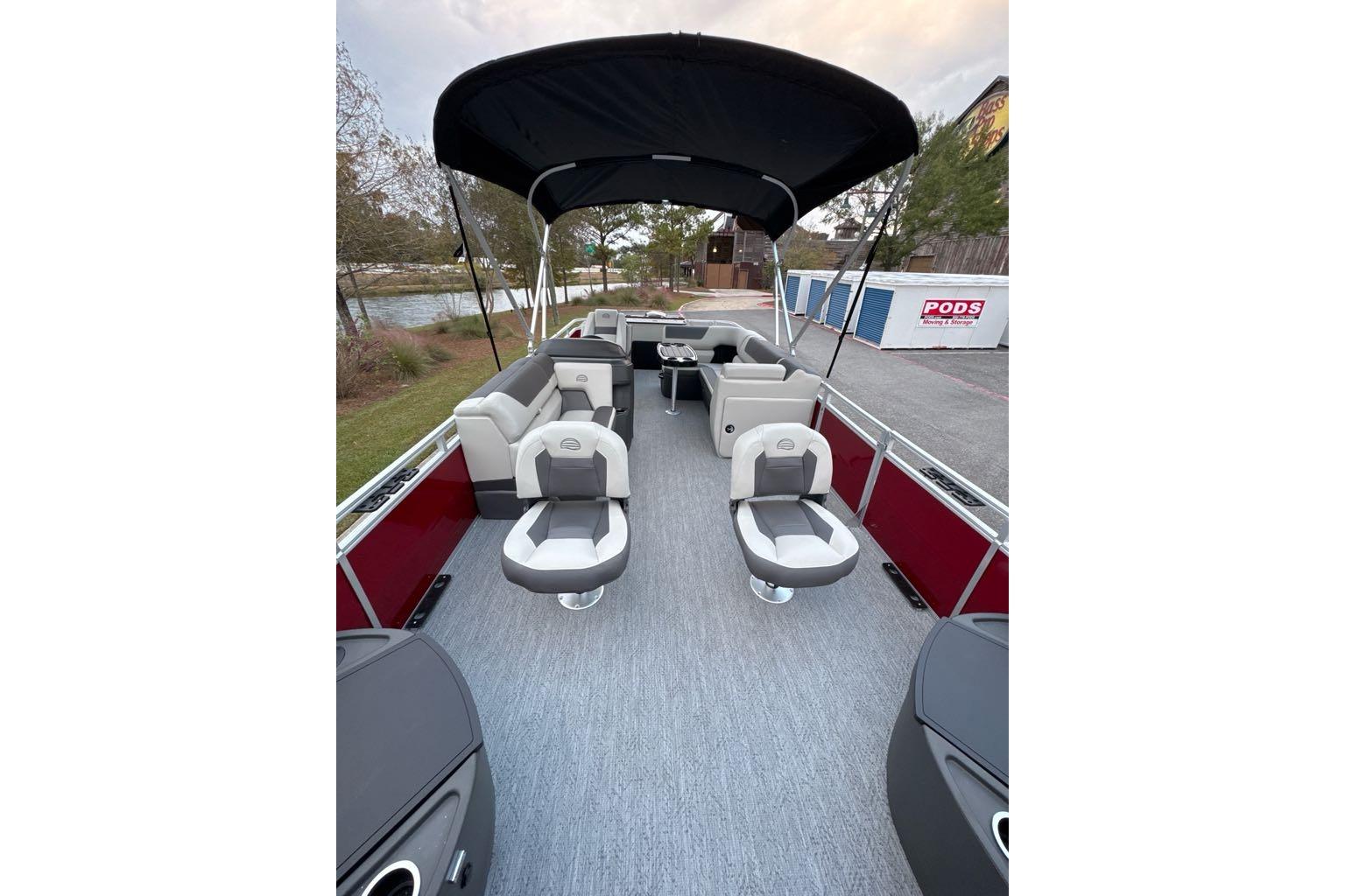 2026 Sun Tracker Fishin' Barge 22 DLX interior with seating and canopy, docked by a lake.