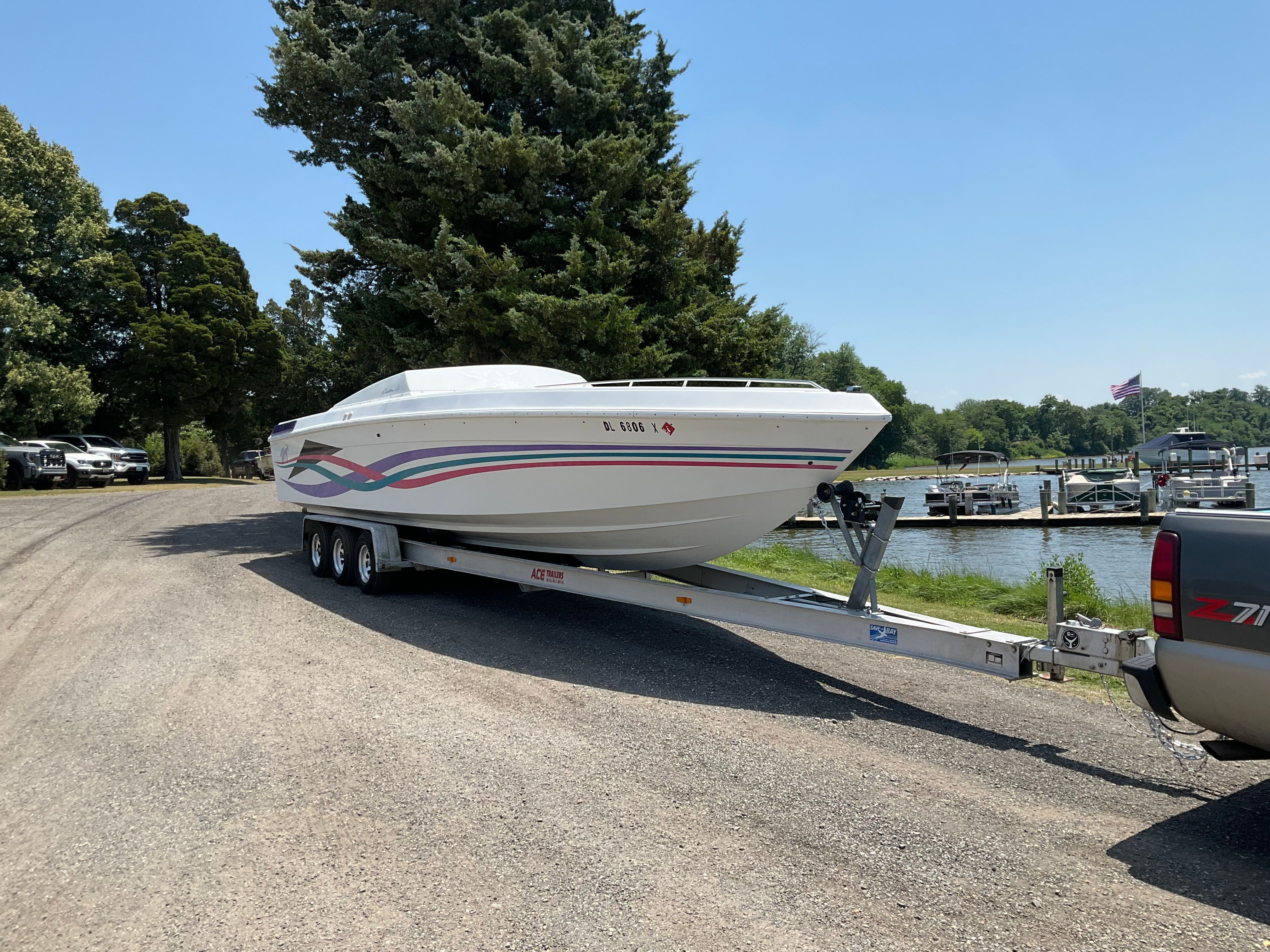 A 1995 Baja Caliber boat on a trailer, parked on a gravel path beside a lake.
