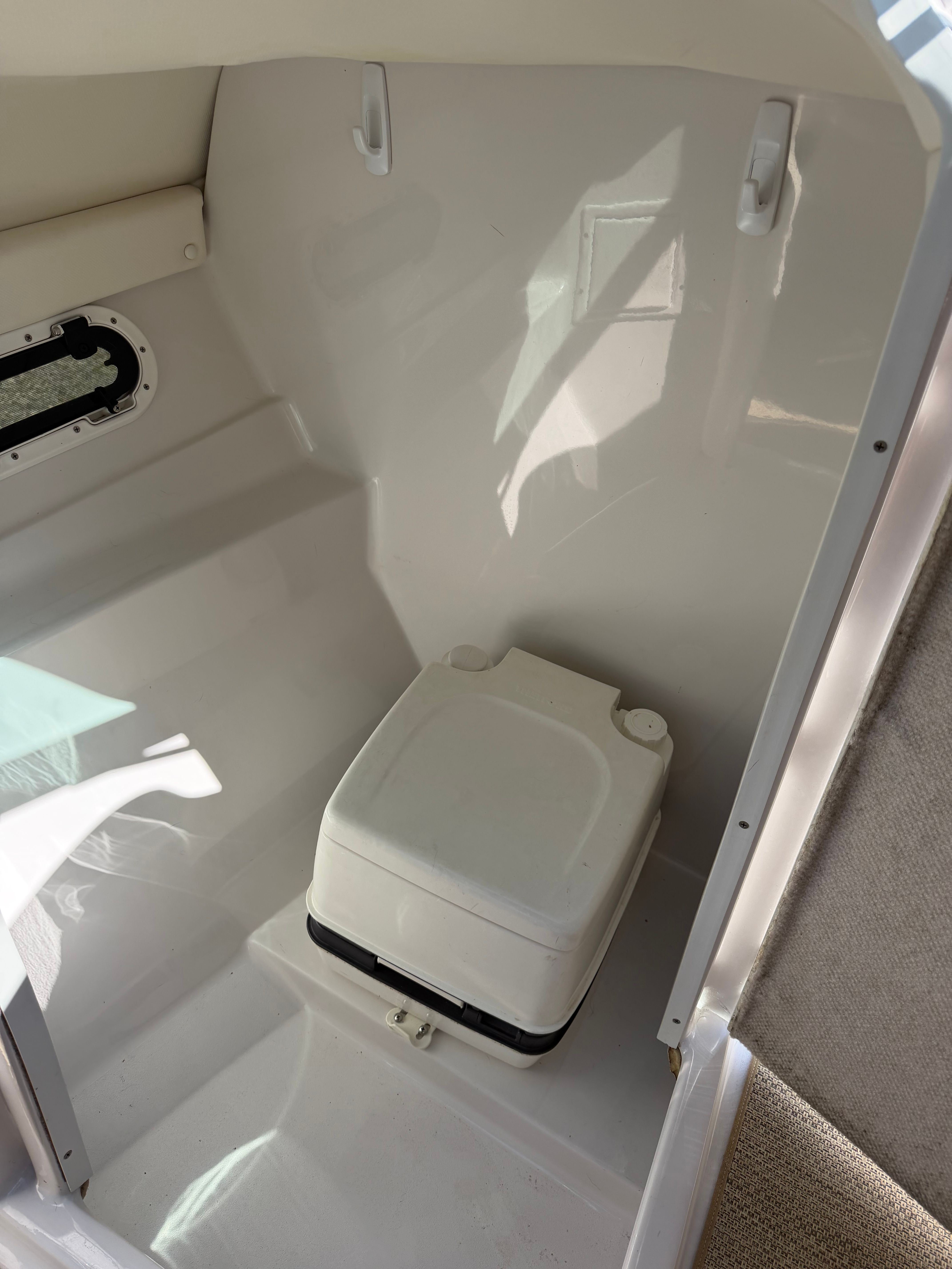 Interior of a boat cabin with a portable toilet and a window.