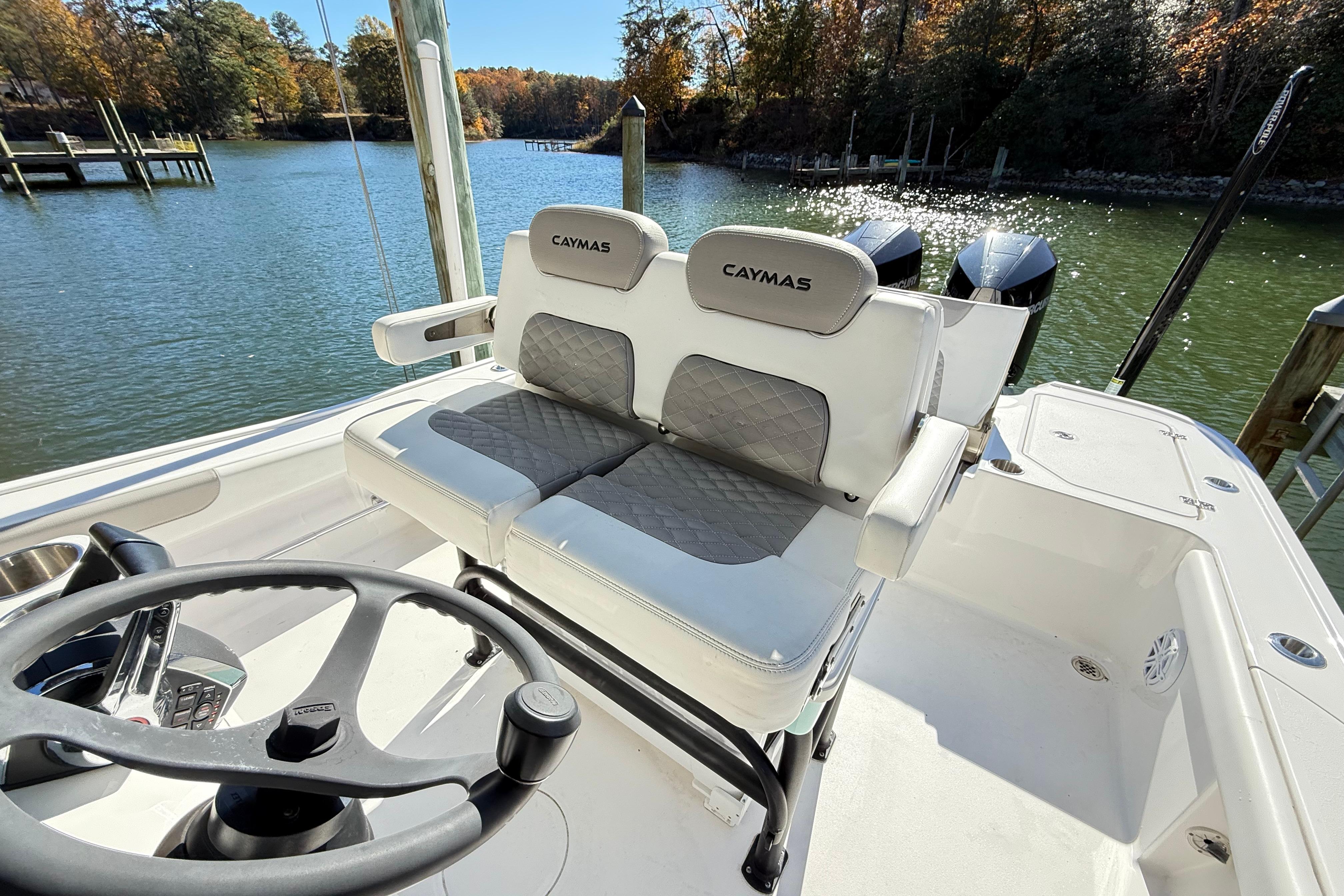 2023 Caymas 281 HB boat interior with dual seats and steering wheel, docked by a scenic lake.