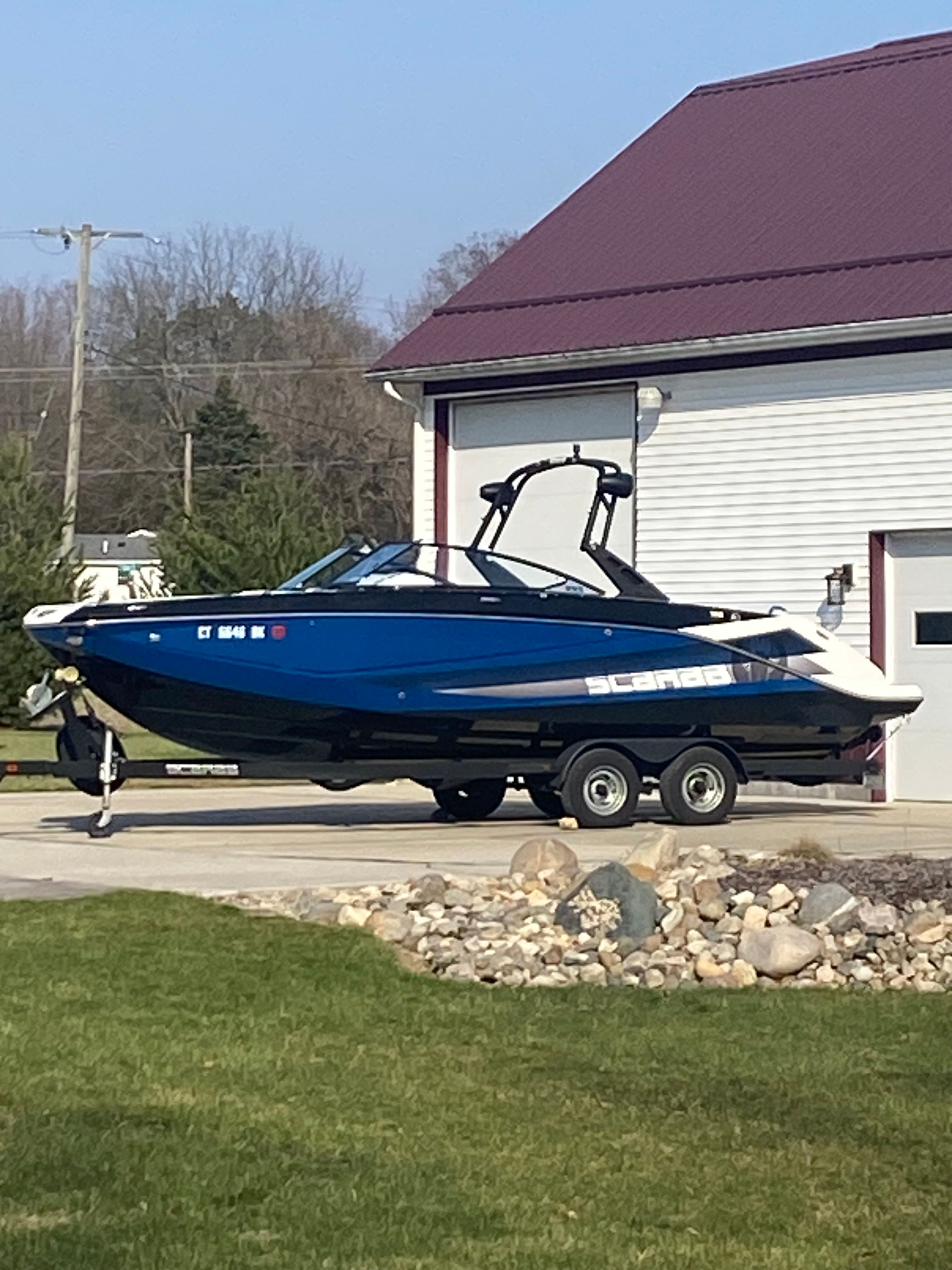 A blue 2018 Scarab 255 HOI on a trailer beside a building.