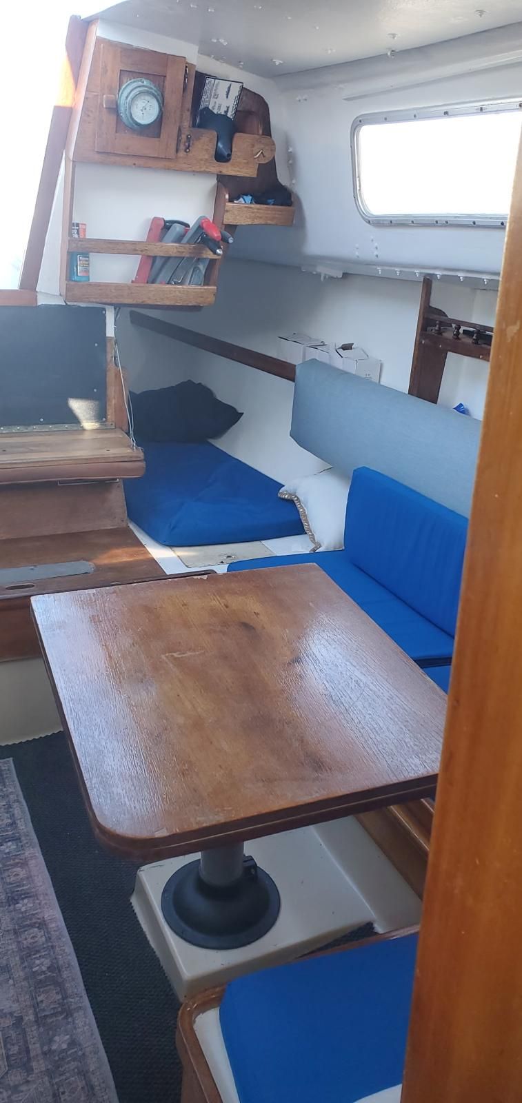 Interior of a sailboat with wooden table, blue cushions, and shelves.