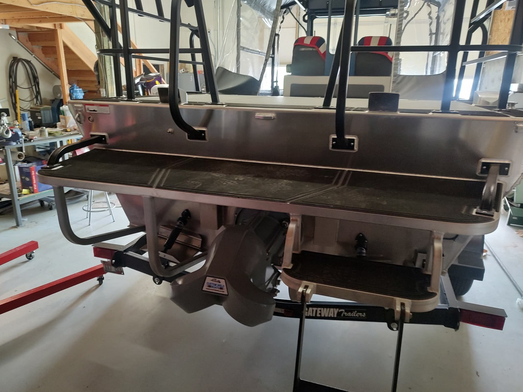The image shows the rear of a Custom Weld 23' sled t-top boat in a workshop.