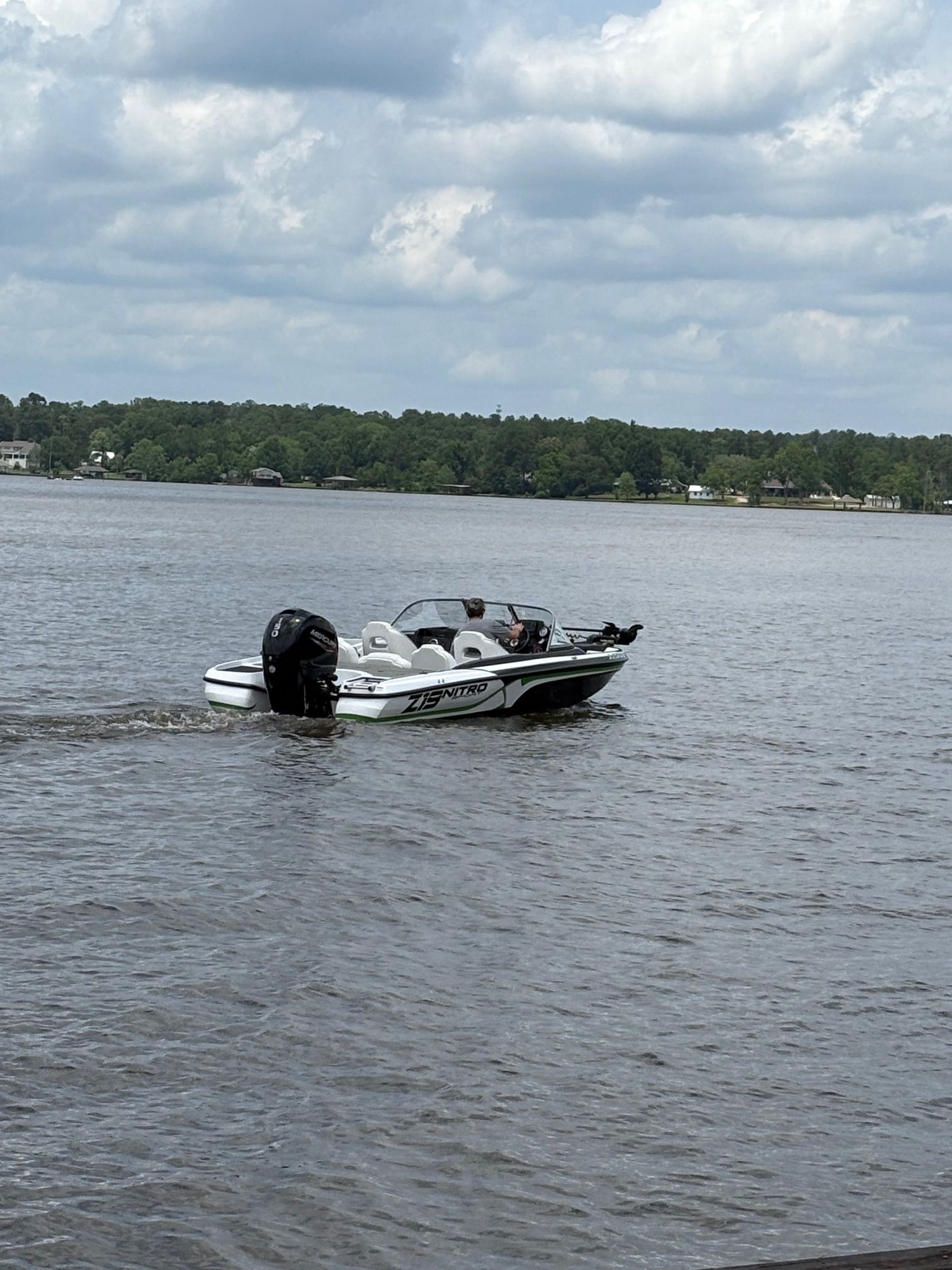 A white motorboat cruises on a calm lake with a wooded shoreline in the background.