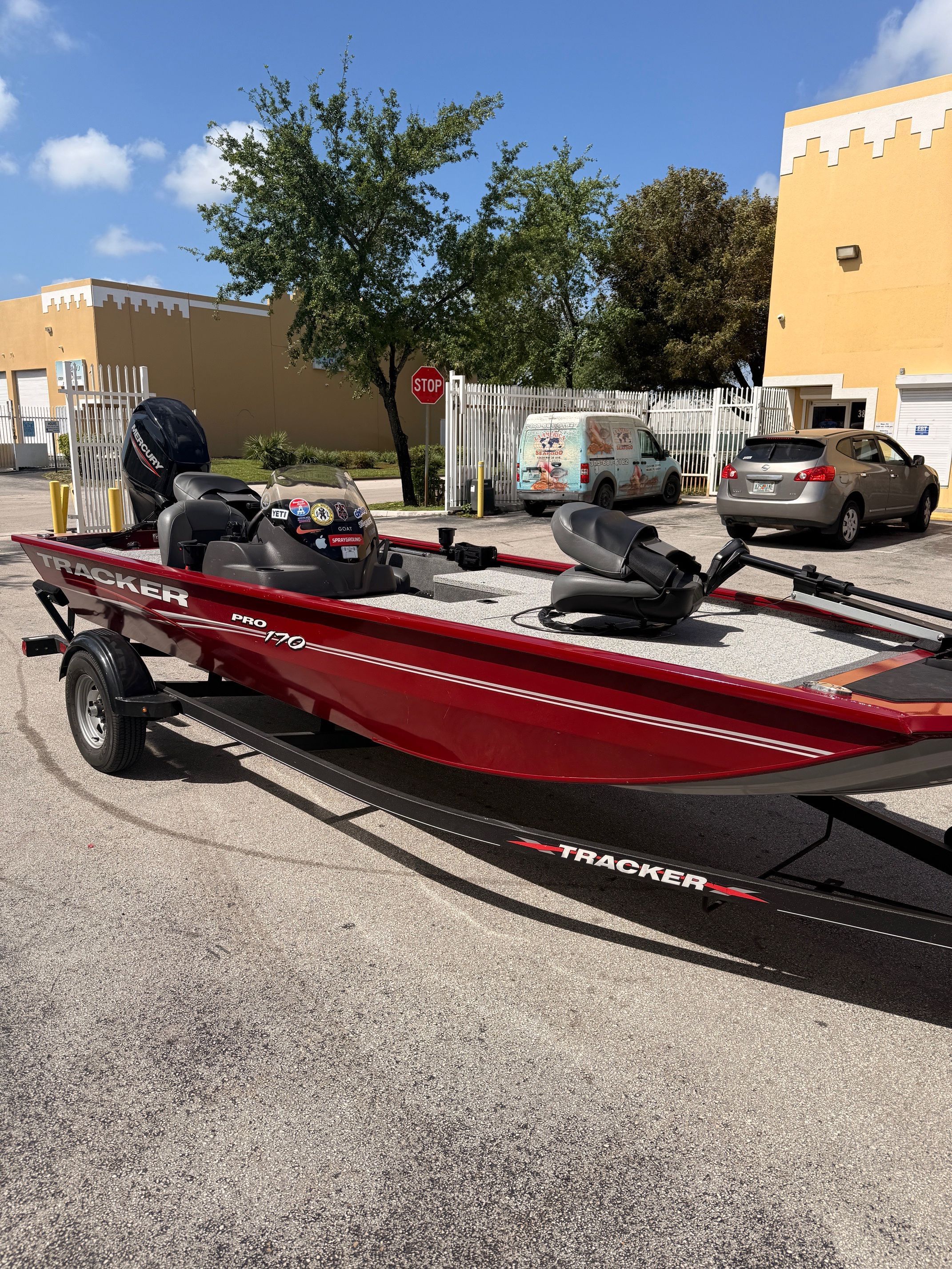 A red Tracker Pro 170 boat on a trailer in a parking lot.