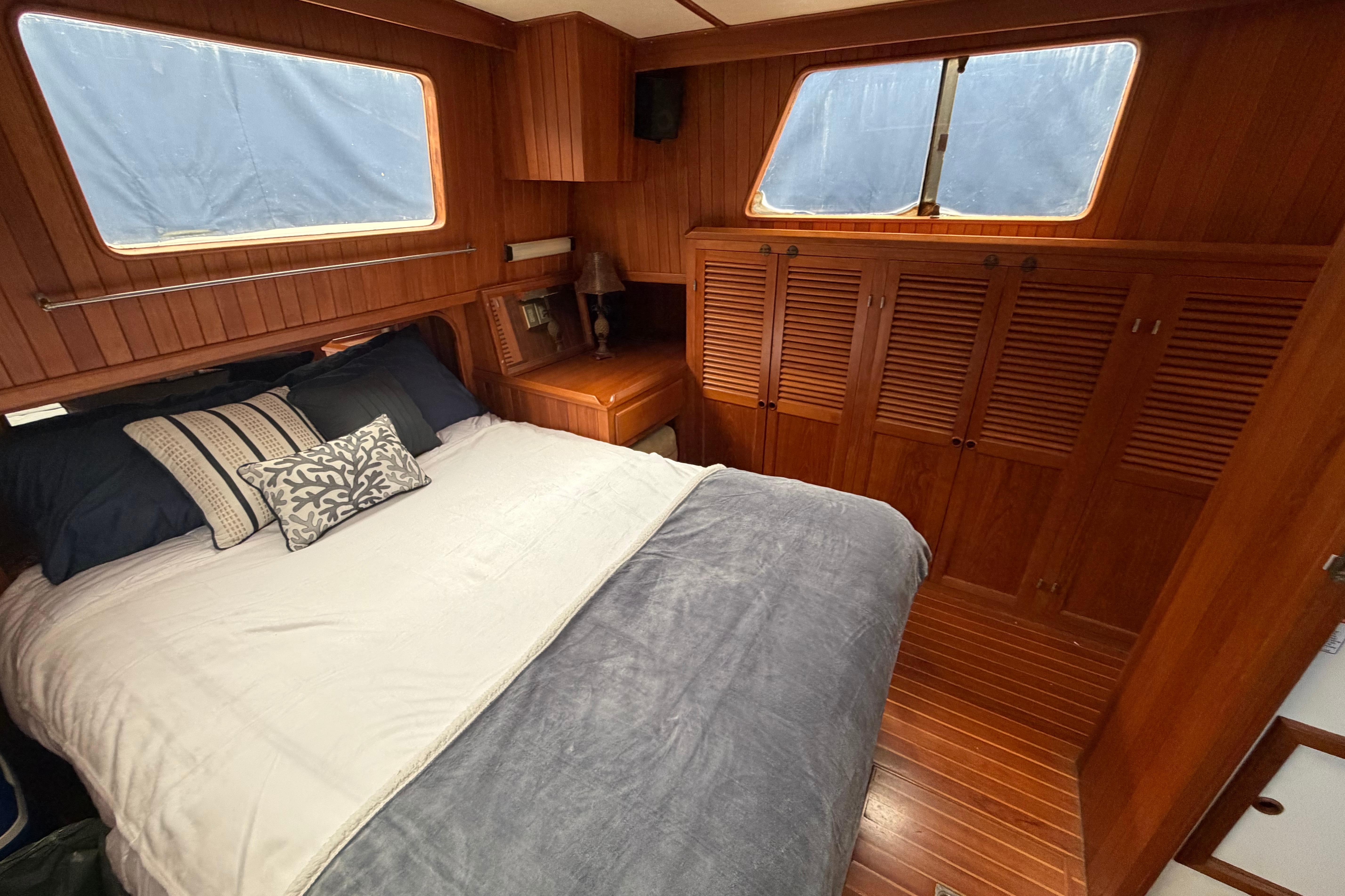 Cozy bedroom in 1988 Monk 36 yacht with wooden interior and large windows.
