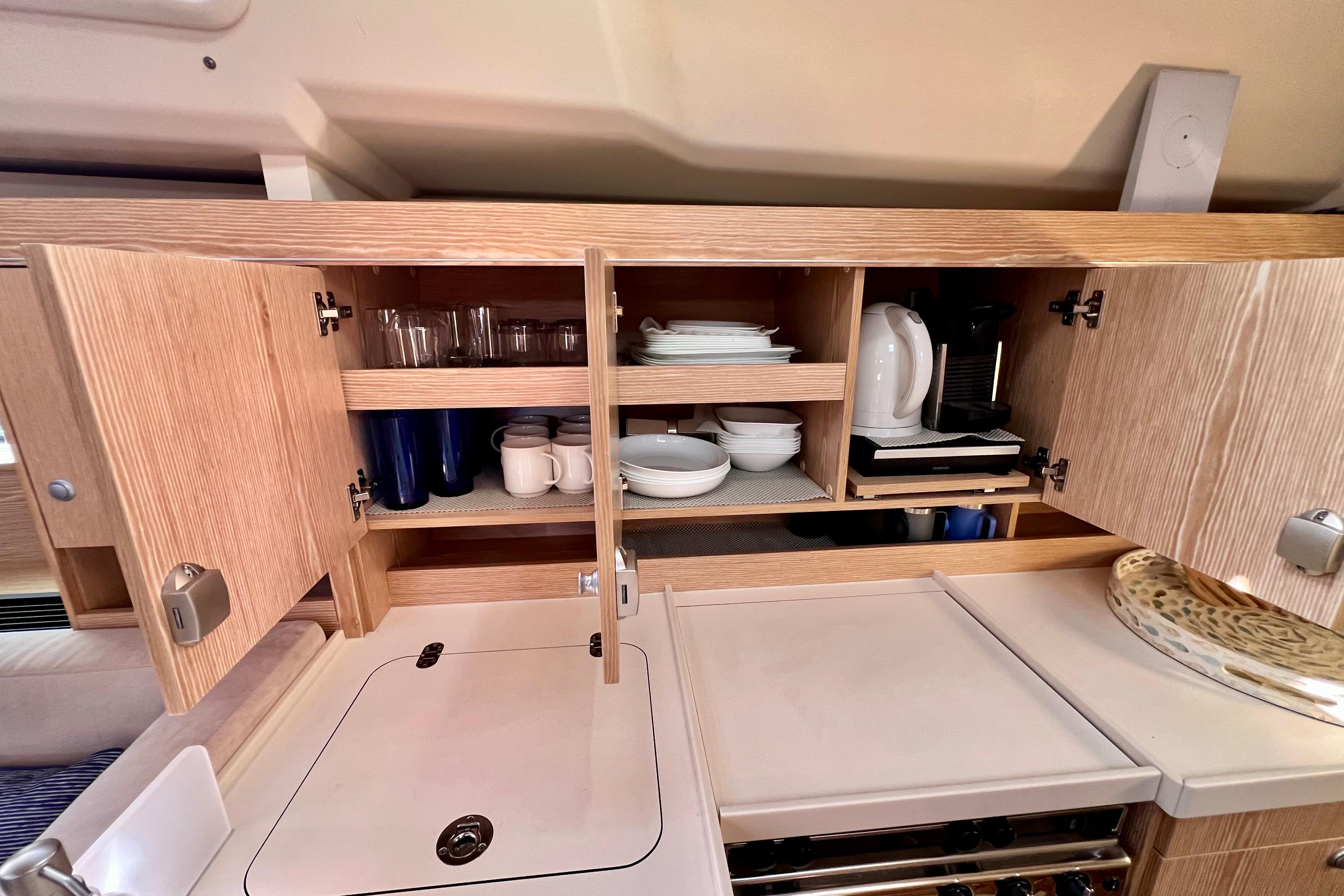 Interior of 2016 Hanse 455 yacht kitchen with open cabinets displaying dishes and appliances.
